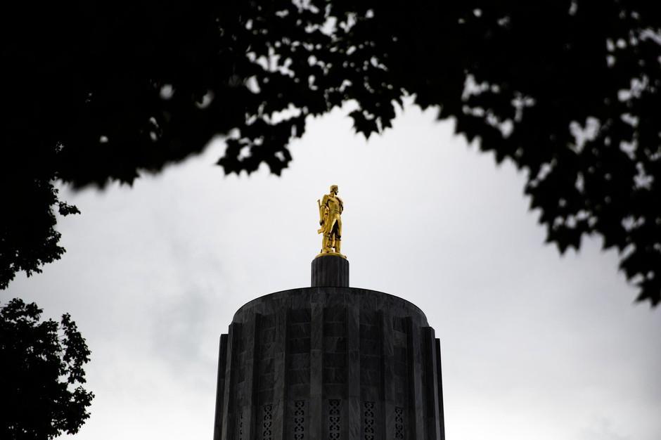 A golden statue of a person perches atop the top of the exterior of the Oregon Capitol in Salem.