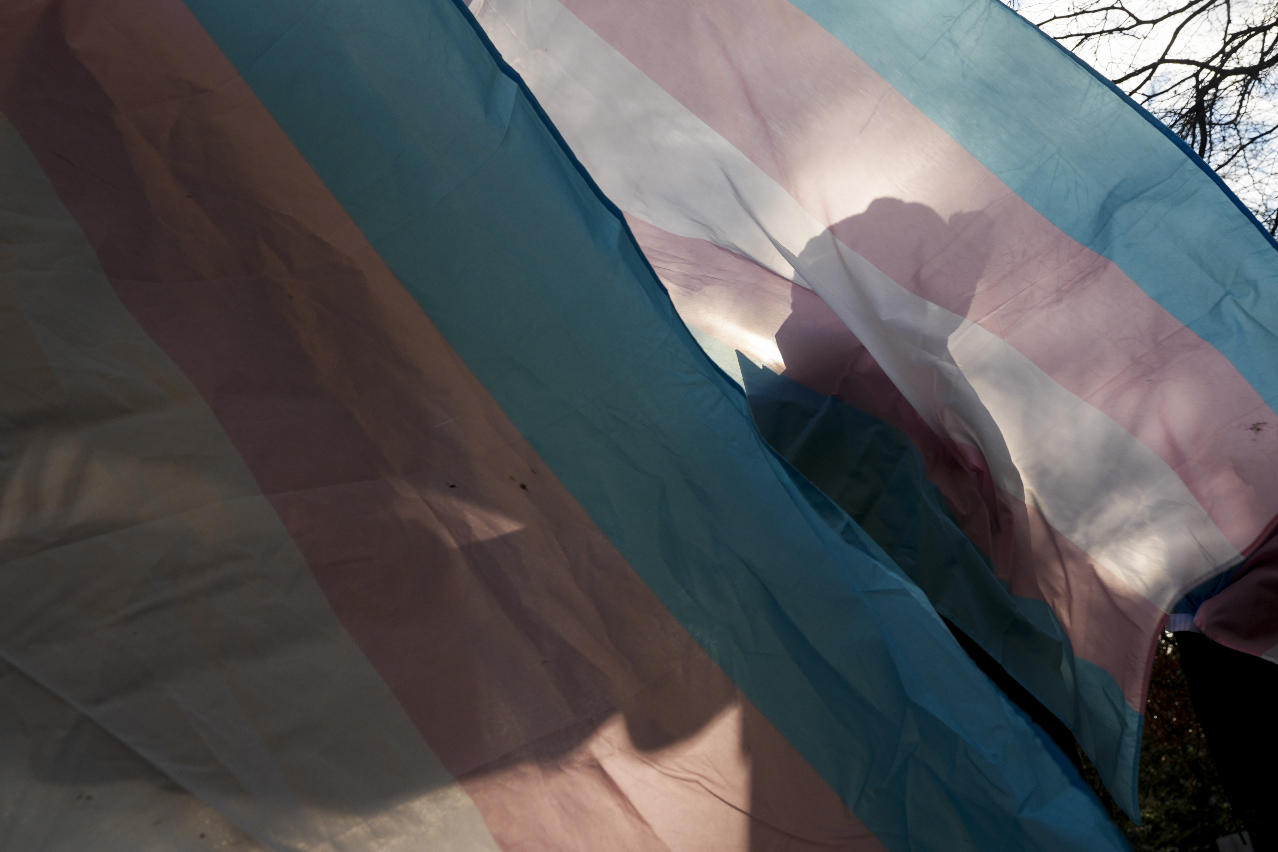FILE - A protester is silhouetted against a trans pride flag during a pro-transgender rights protest in April. Kaiser Permanente has announced they will pause gender-affirming surgeries for patients under 19.