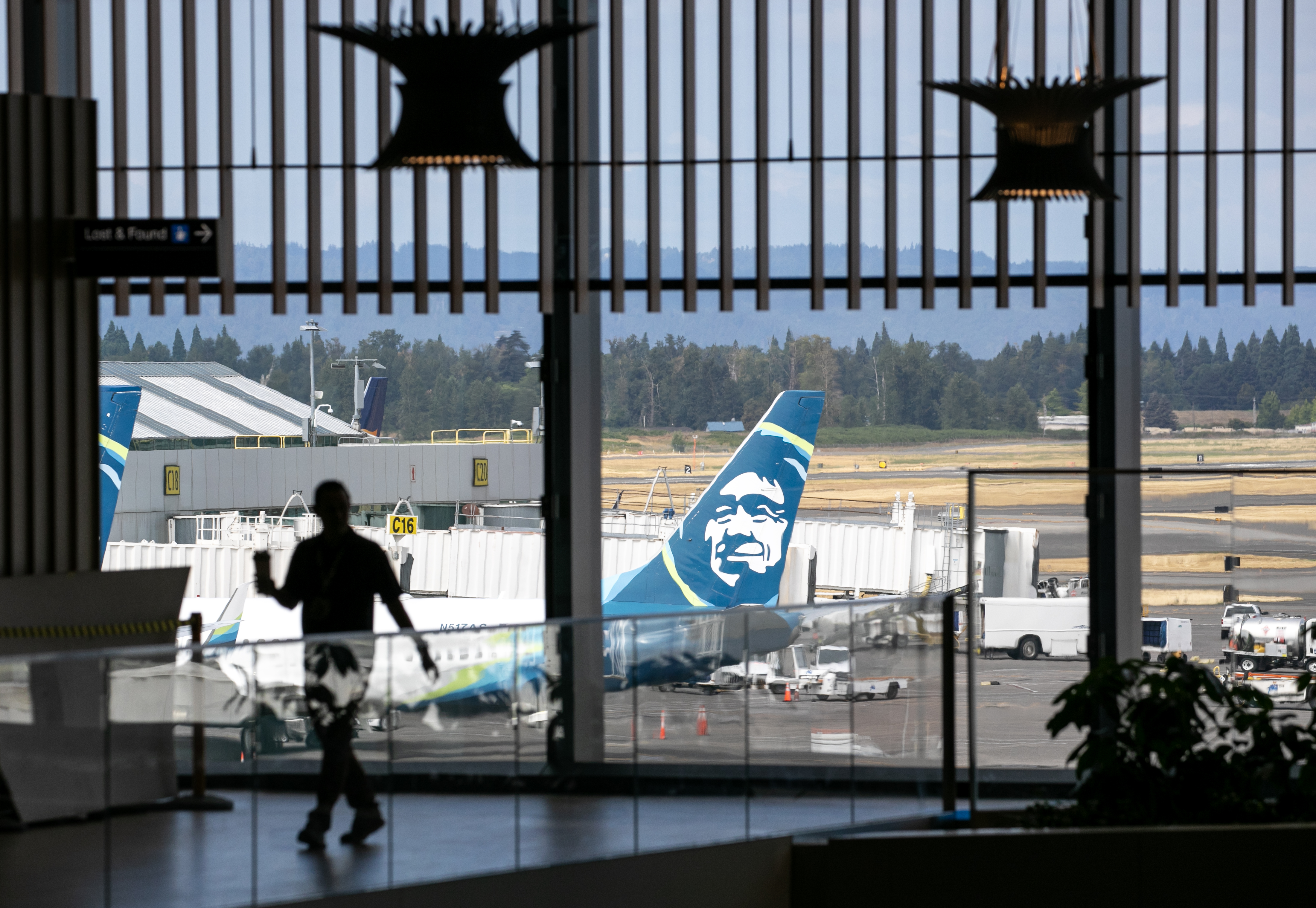FILE - A person walks on the upper mezzanine of Portland International Airport's main terminal, with an Alaska Airlines plane in the background, Aug. 14, 2024. 