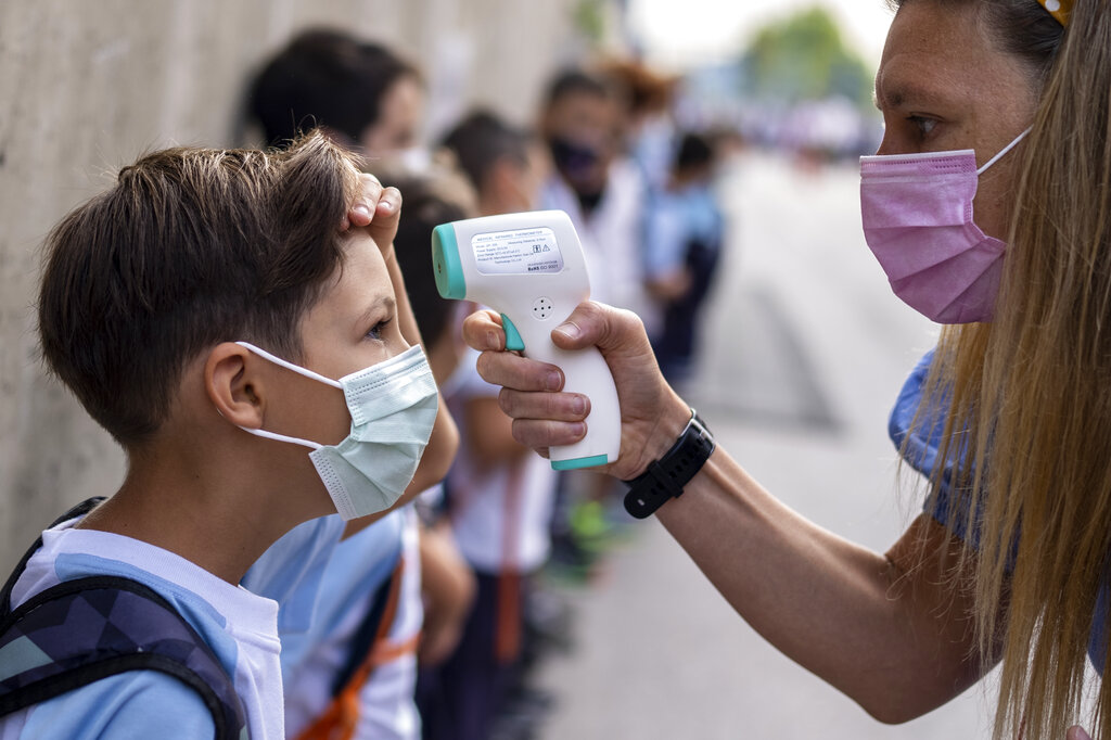 A teacher wearing a face mask to protect against the spread of coronavirus checks the temperature of her student.