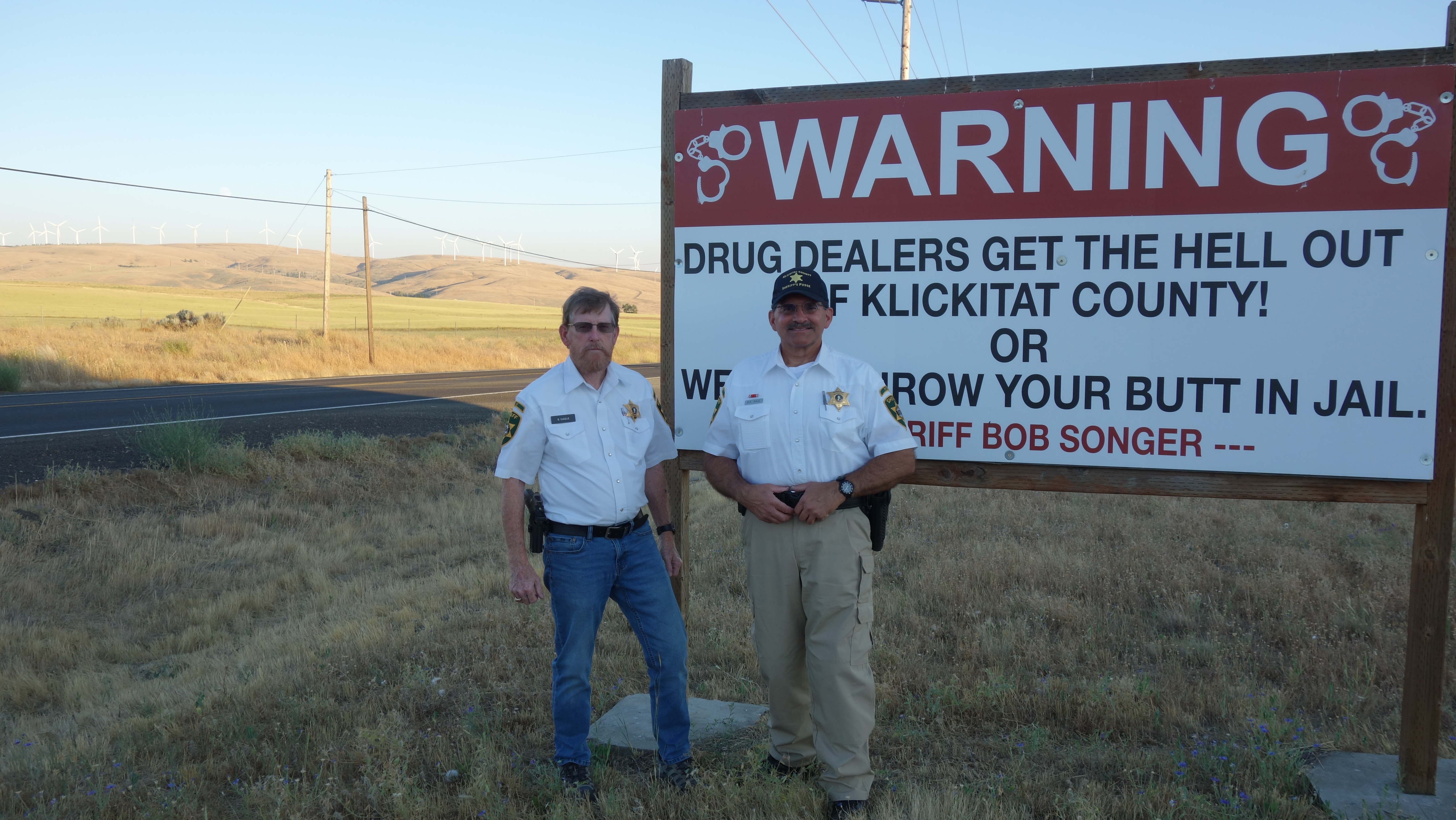 Klickitat County Sheriff’s Posse members Shane Cagle, left, and Brian Paul stand in front of a sign that greets people at the county line.