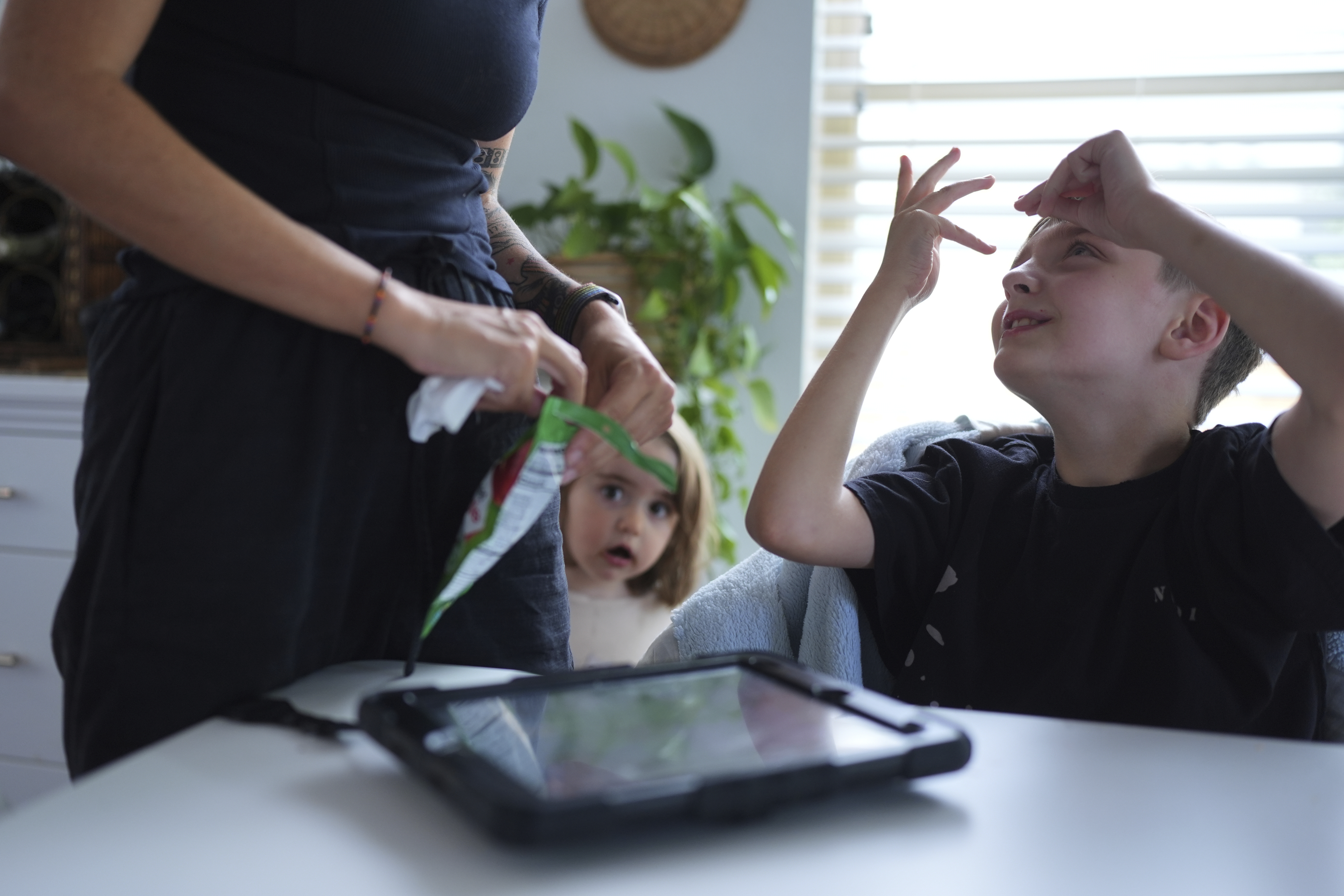 Charlie Lamb, right, who is diagnosed with autism and is non-verbal, uses an AAC device to communicate with his mother Eileen Lamb left, who also has autism, as Charlie's sister Billie looks on, Monday, May 12, 2025, in Austin, Texas.