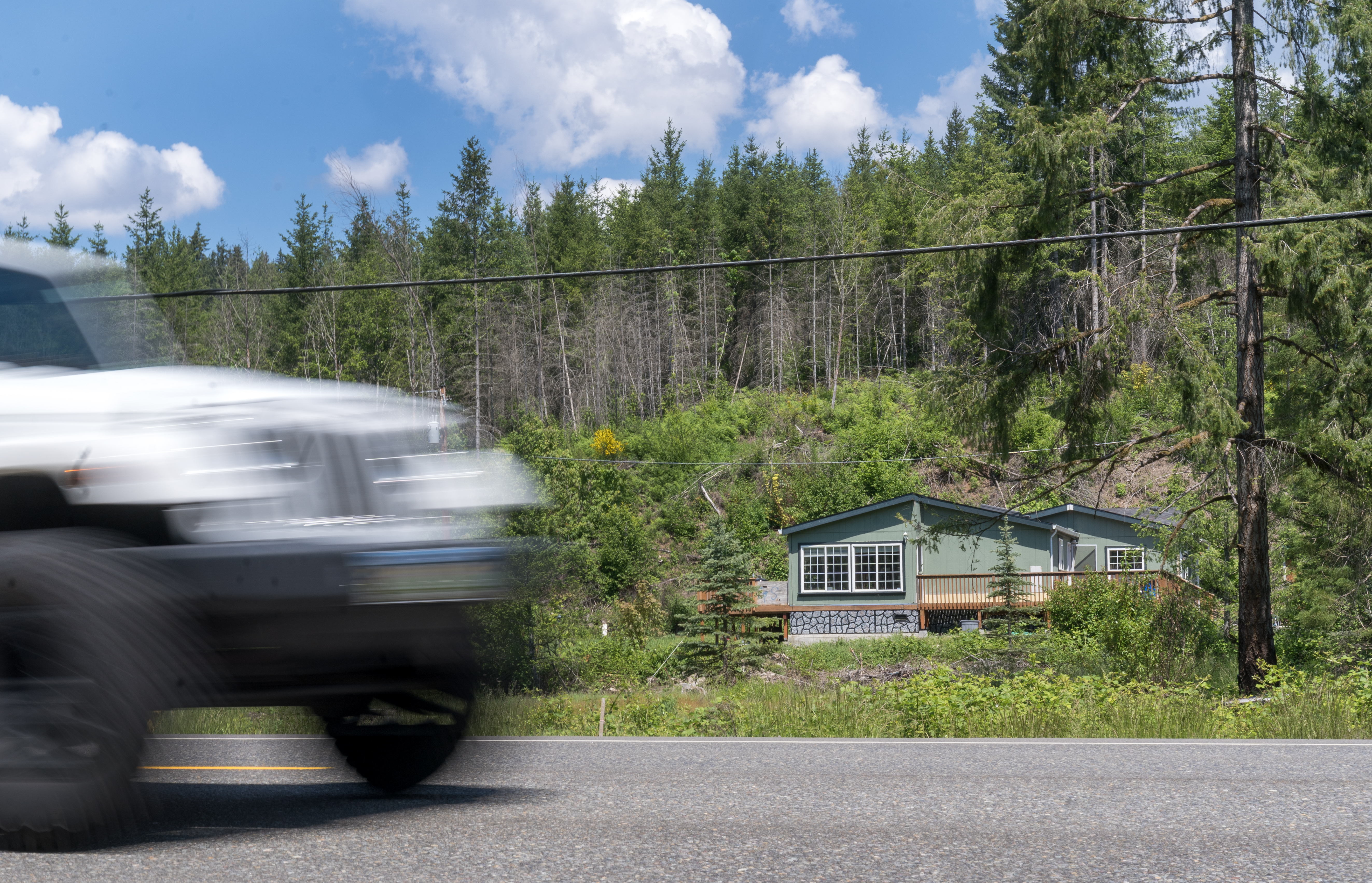 Traffic speeds by on Highway 18 in front of Bill Edge’s rebuilt home in Gates, May 26, 2023. “We could never hear the road. We had big trees along the whole road out there. It looked like a park in here,” said Edge.