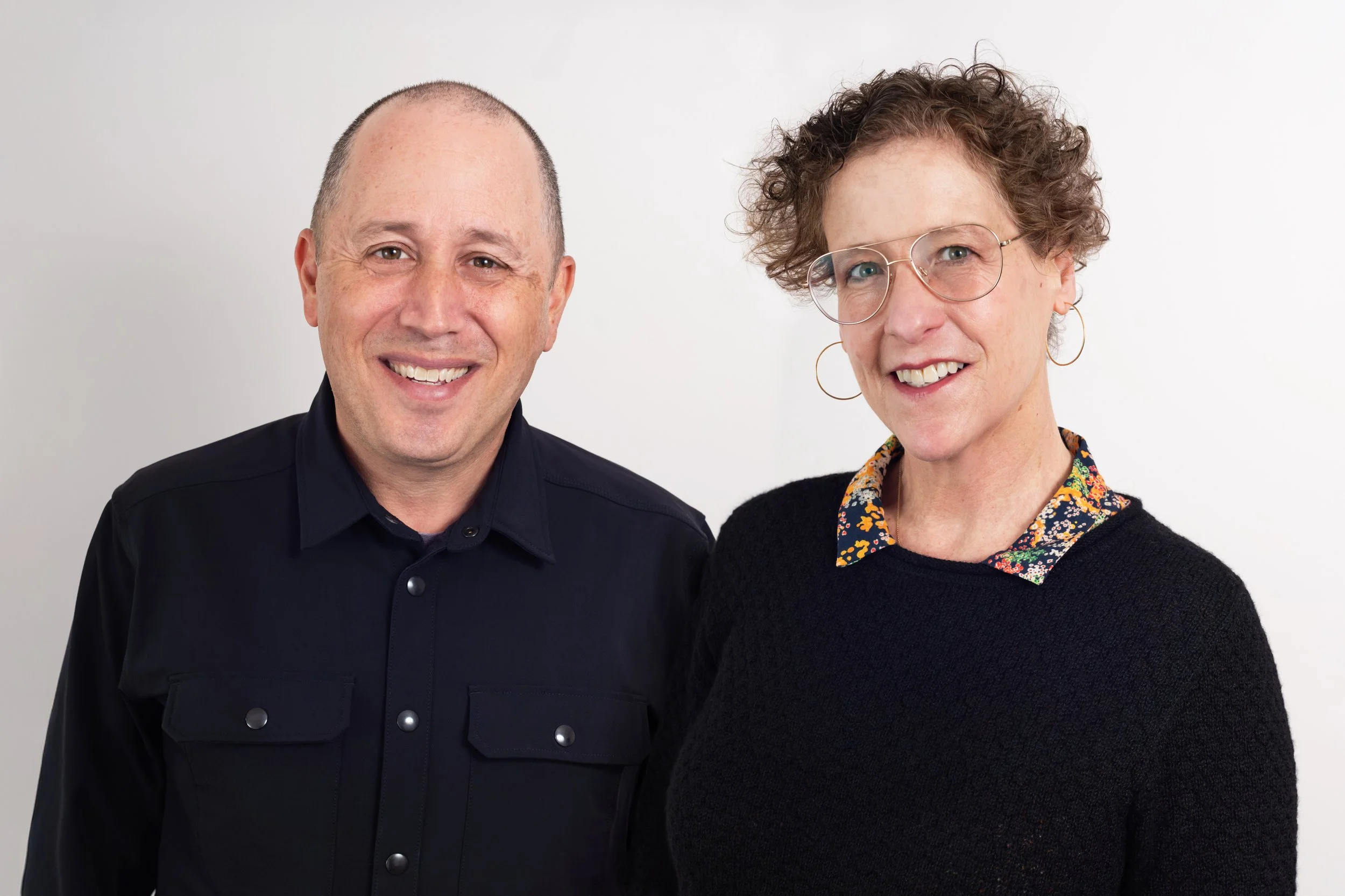 Two people standing in front of white wall in sweaters
