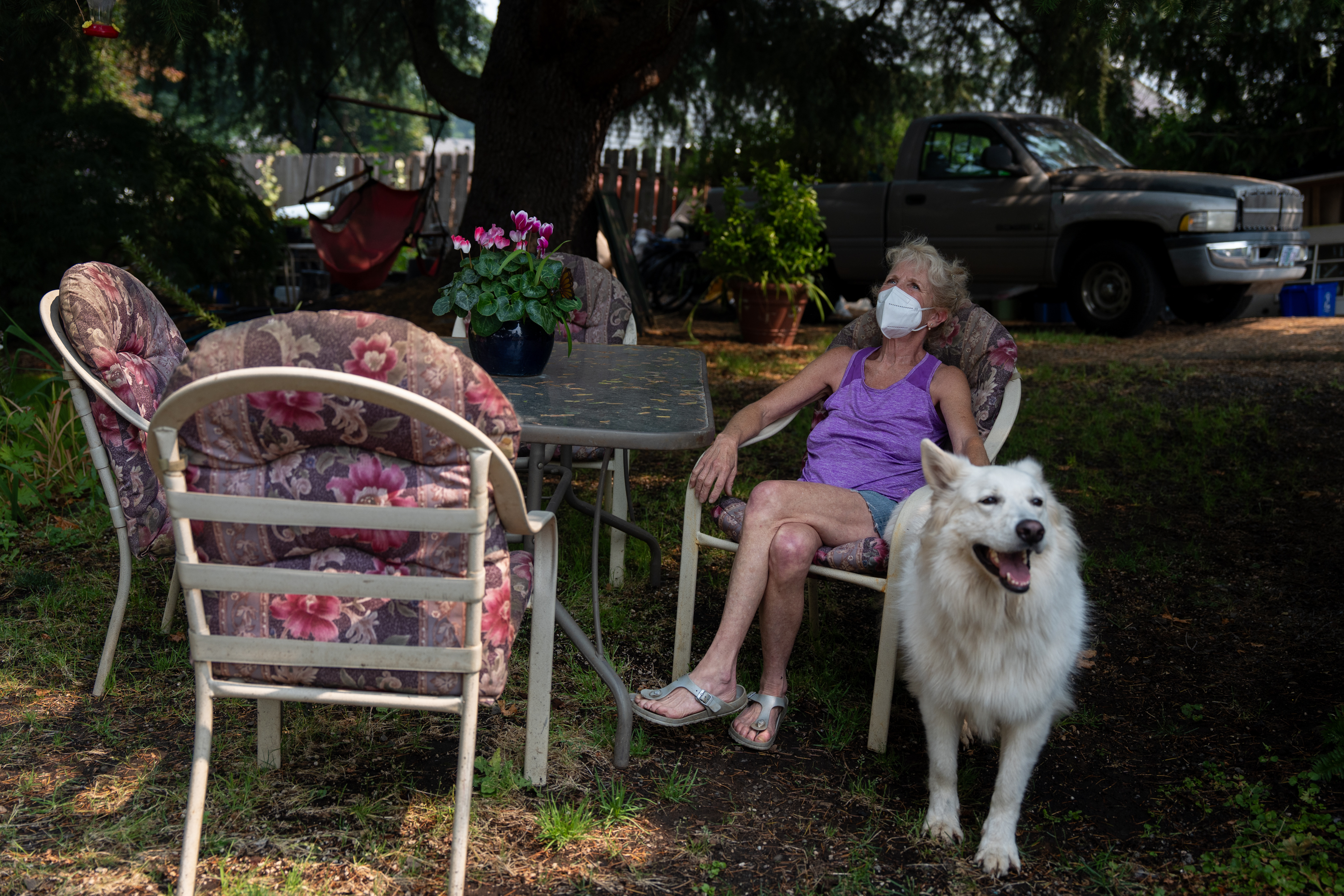 Fawnda Buck looks up to the smokey sky, wearing a KN95 mask her neighbor gave her, as she rests in the yard of her home Airbnb, accompanied by one of her dogs, Porsche, in Sandy, Ore., on Aug. 5, 2026.