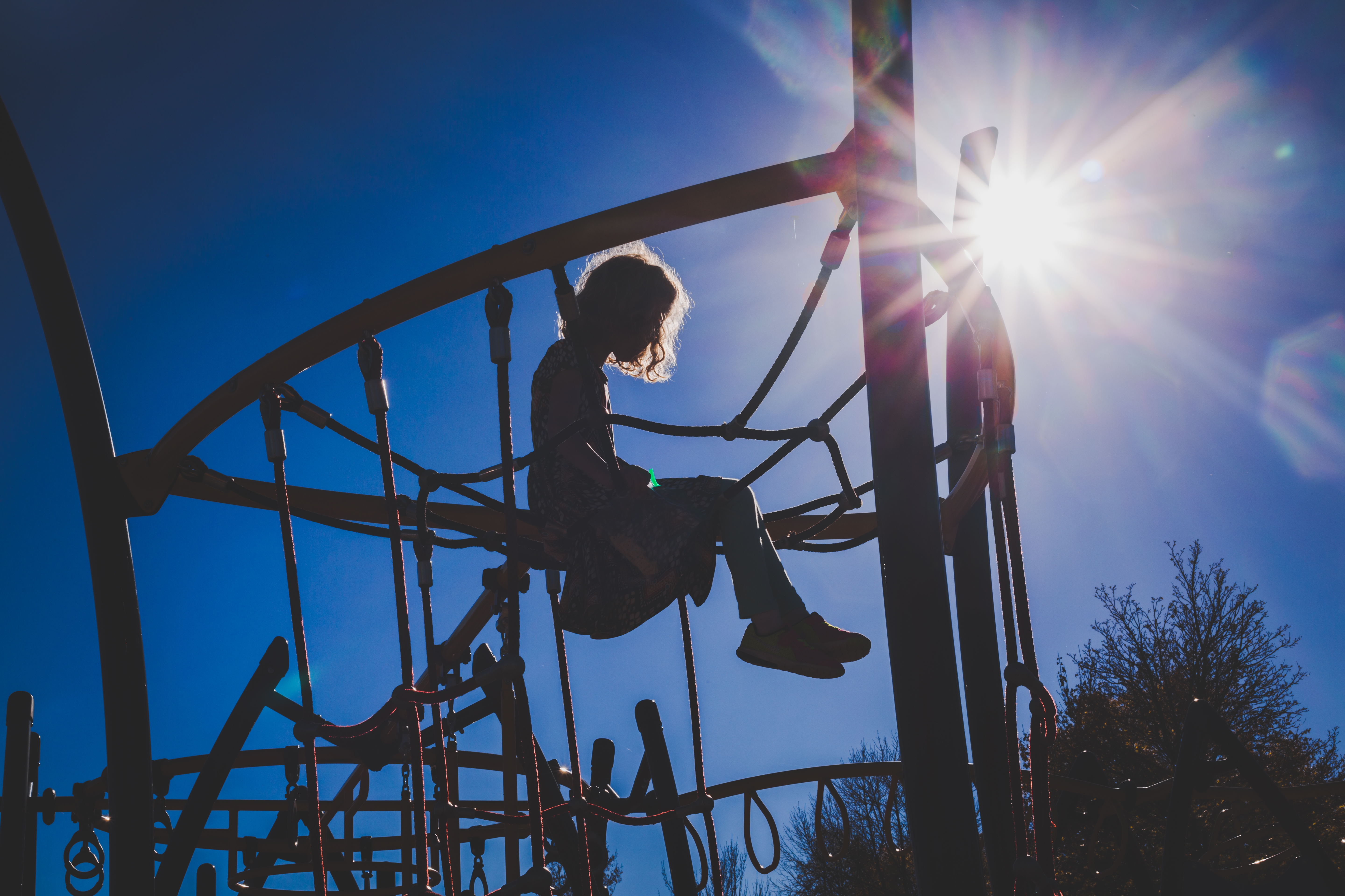 Little girl with curly hair sits on top of a playground jungle gym.