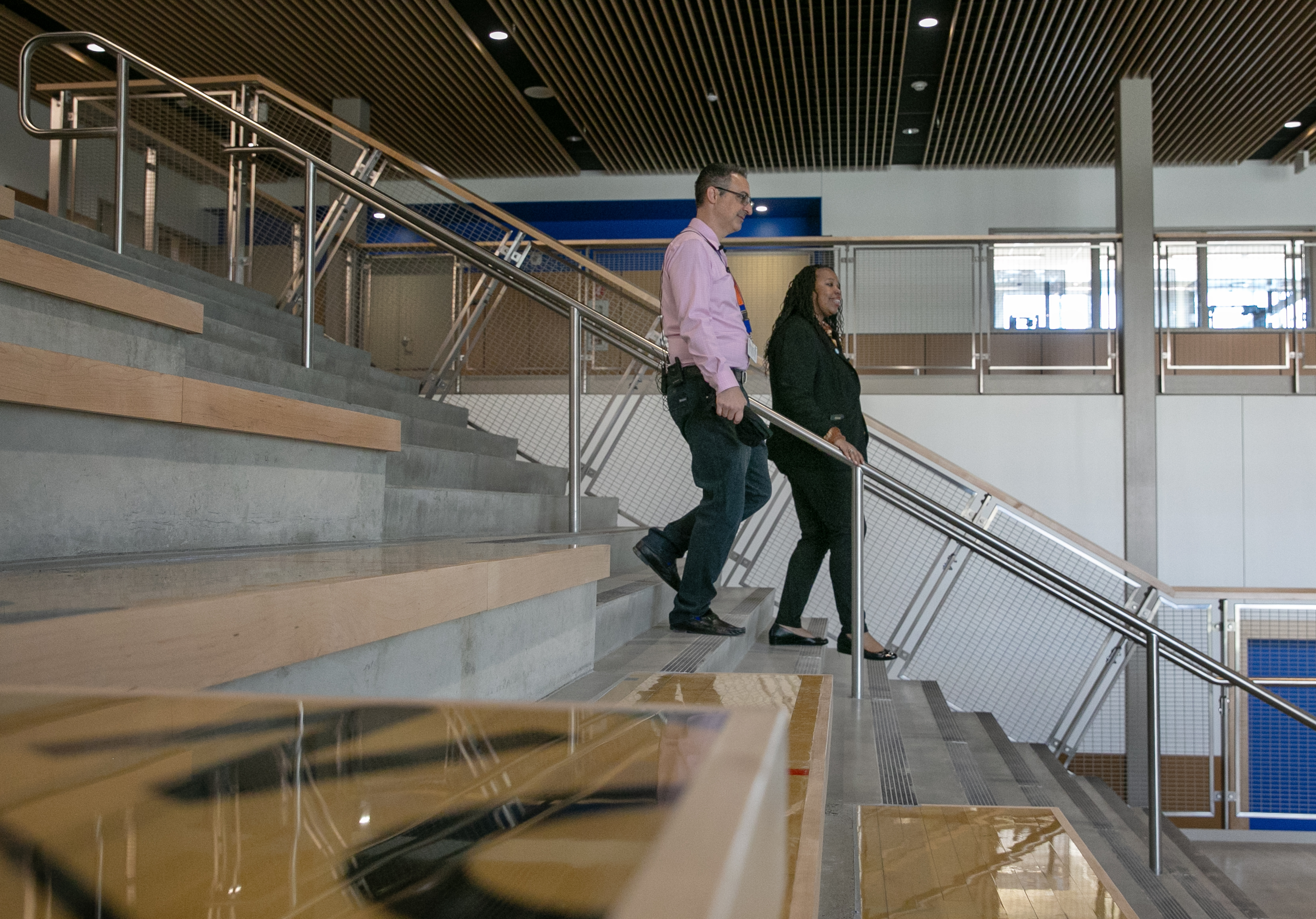 Portland Public Schools Director of Construction Armand Milazzo, left, leads new superintendent Kimberlee Armstrong through the remodeled cafeteria of Benson Polytechnic High School, Portland, Ore., Aug. 27, 2024. In the foreground, repurposed lumber from the building's old gymnasium has been repurposed into seating. Care was taken throughout the renovation process to preserve as much of the century-old building's original character as possible. 