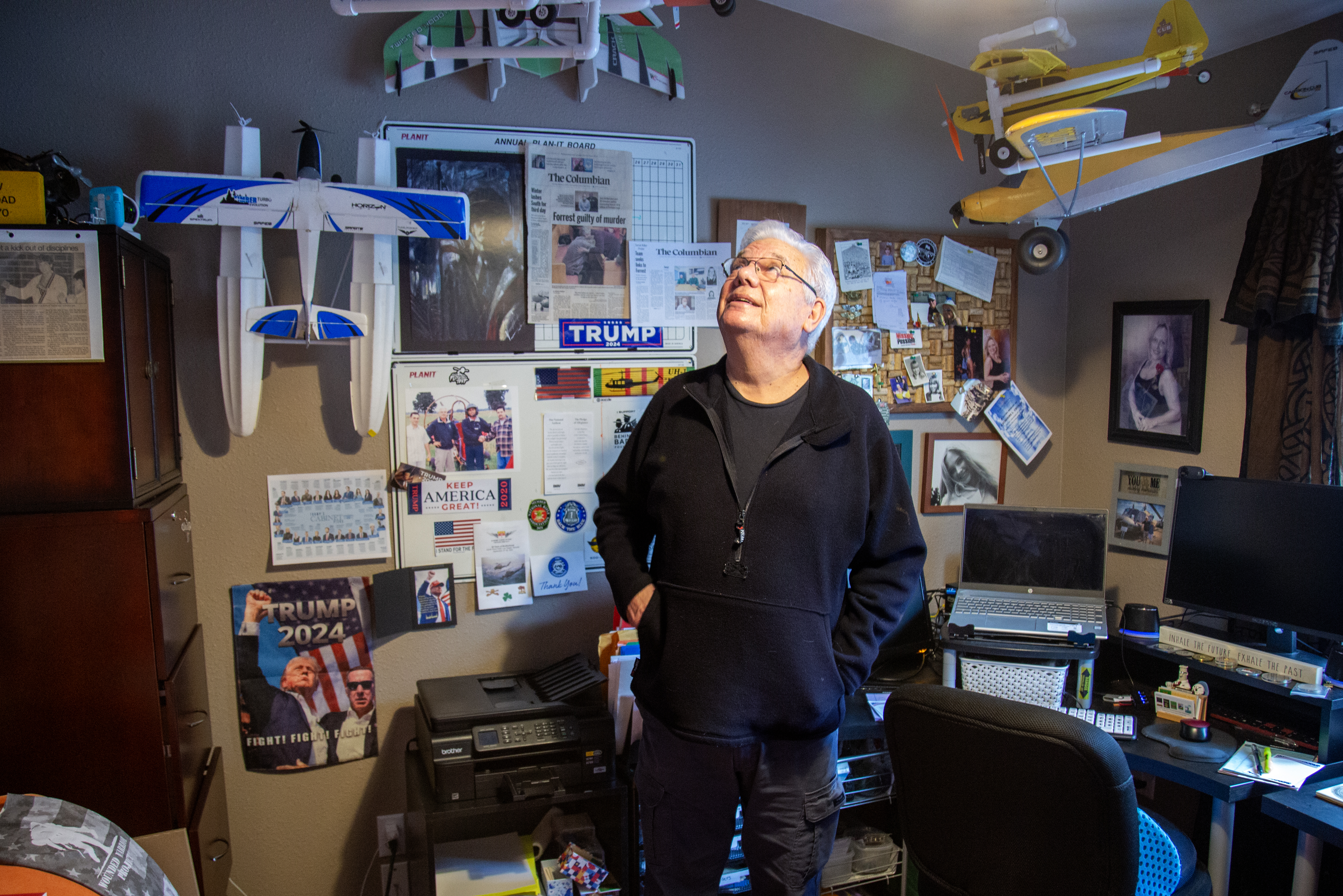 A man stands in an office with posters and model airplanes on the walls and ceiling.