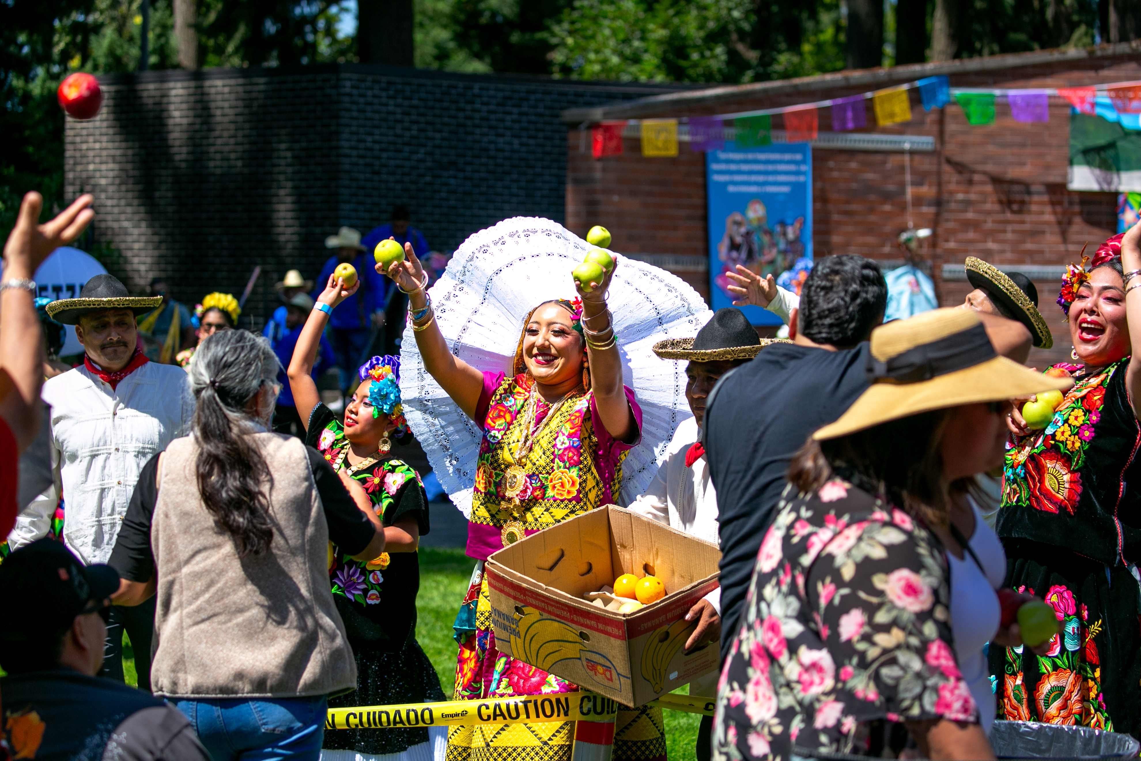 Performers with Alma Oaxaqueña toss fruit to La Guelaguetzaattendees following their dance in Shute Park in Hillsboro, Ore., Aug. 9, 2025. La Guelaguetza is a an annual indigenous event aimed to celebrate indigenous culture and provide a sense of belonging among the community filled with traditional food, dances and music.