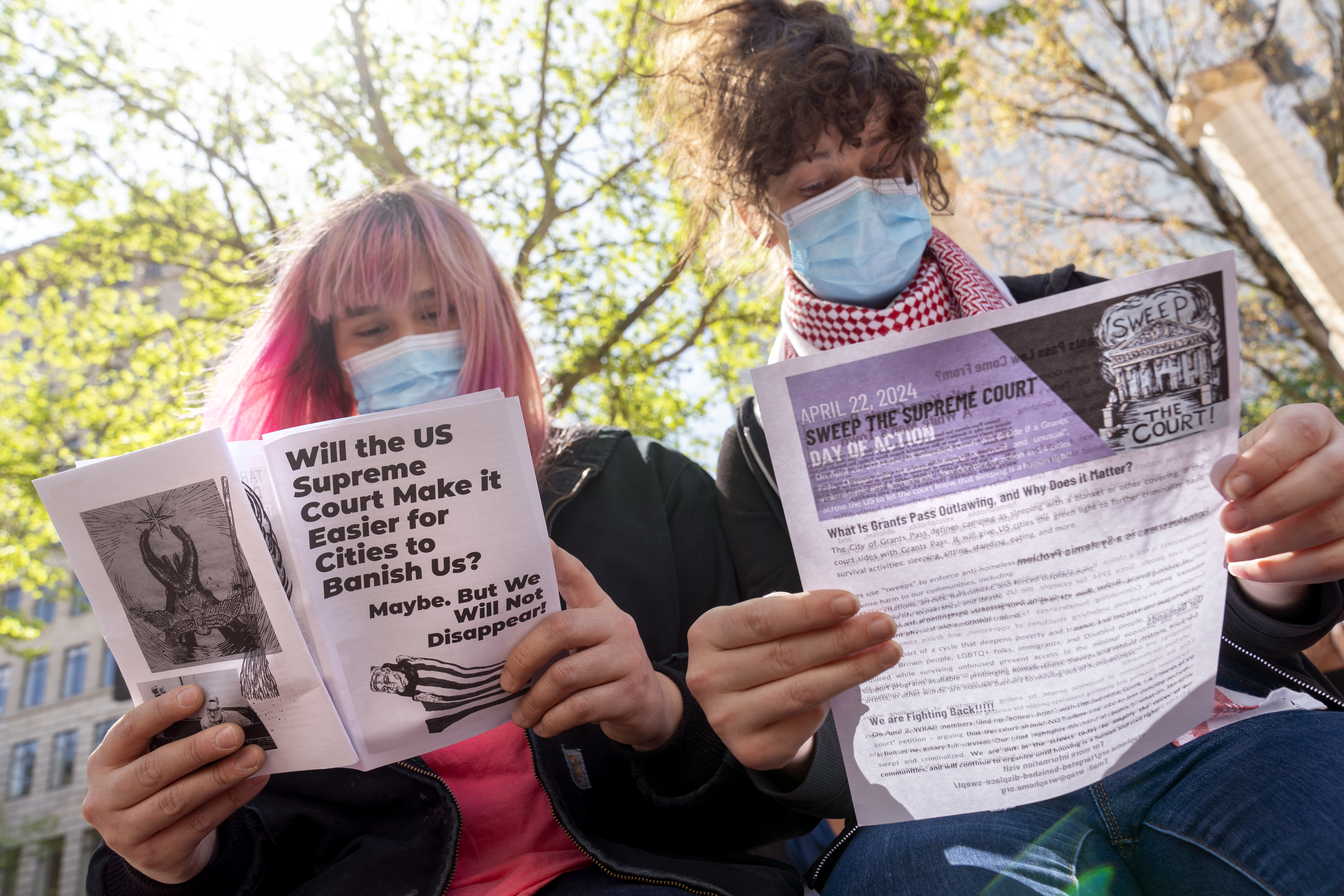 FILE: Mia Rose of Eugene, left, and Samira Jensen of Portland read literature as they attend a rally at Pioneer Courthouse in Portland, Ore., April 22, 2024, organized by Stop The Sweeps PDX. The U.S. Supreme Court sided with the city of Grants Pass on Friday, June 28, 2024, in finding that local governments have the ability to remove outdoor homeless encampments. 