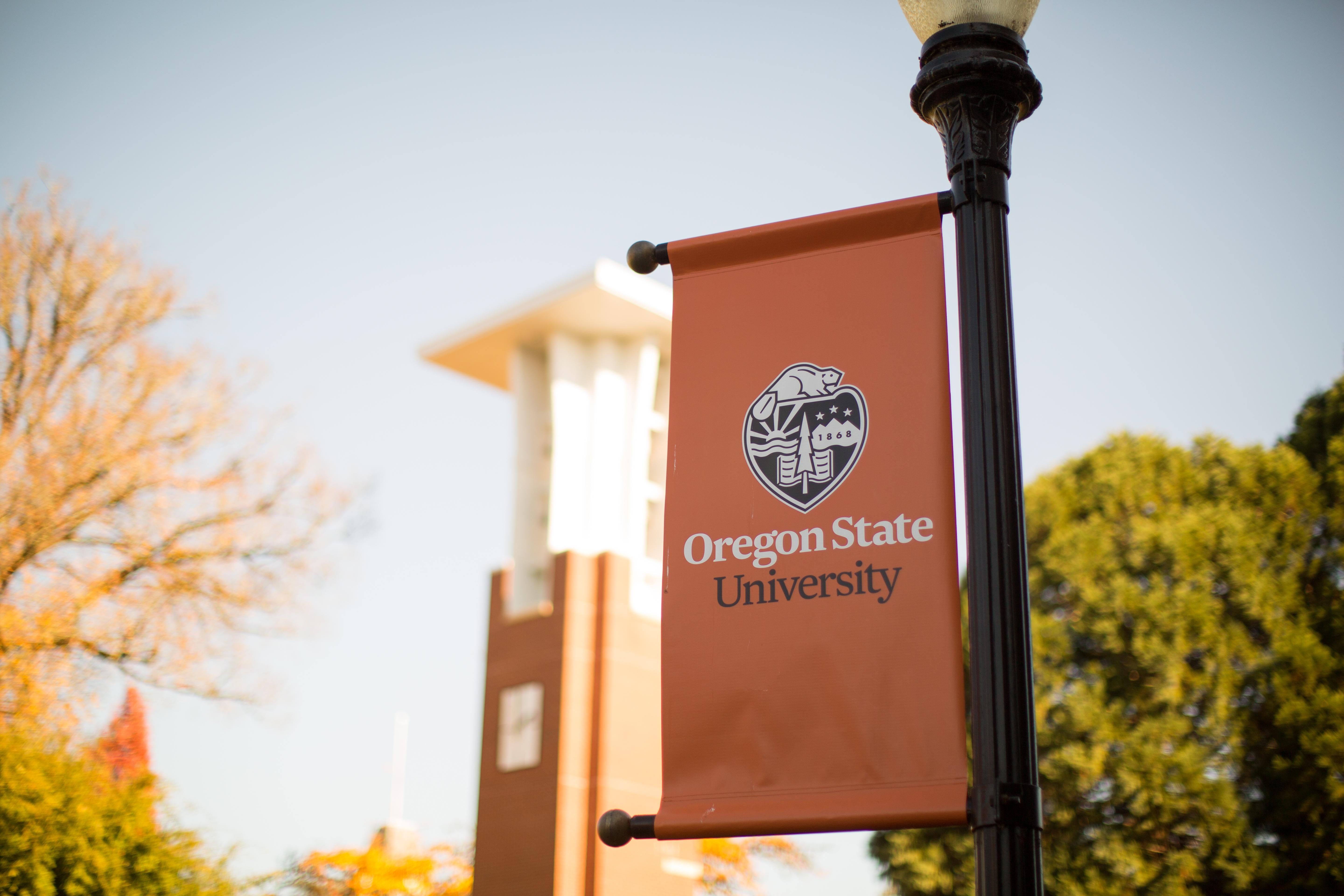 An orange banner affixed to a light pole reads "Oregon State University," while a campus building is visible in the background.