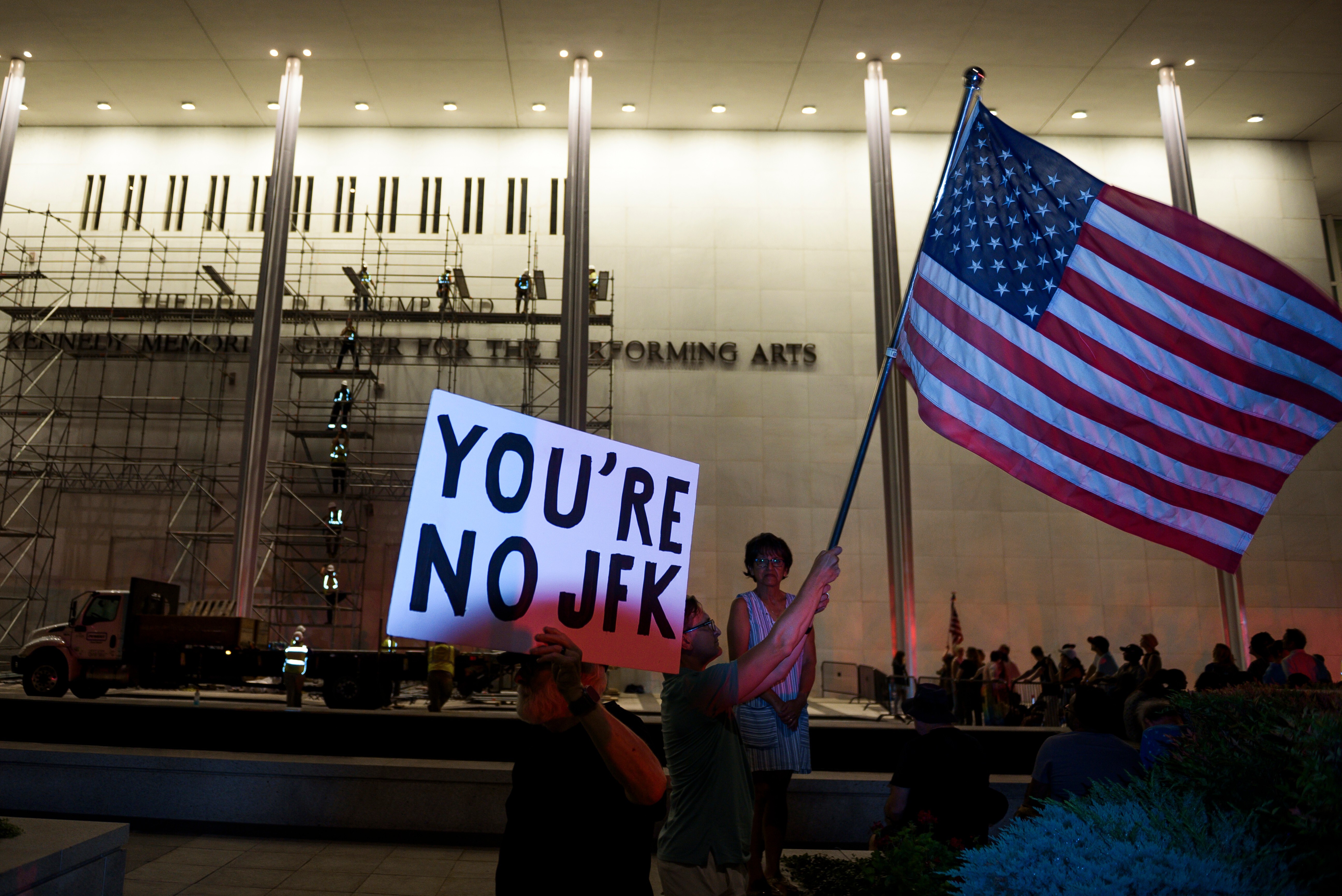 Protestors wave a U.S. and signs as workers prepare to remove President Donald Trump's name from the John F. Kennedy Center for the Performing Arts in Washington, Saturday, June 13, 2026.