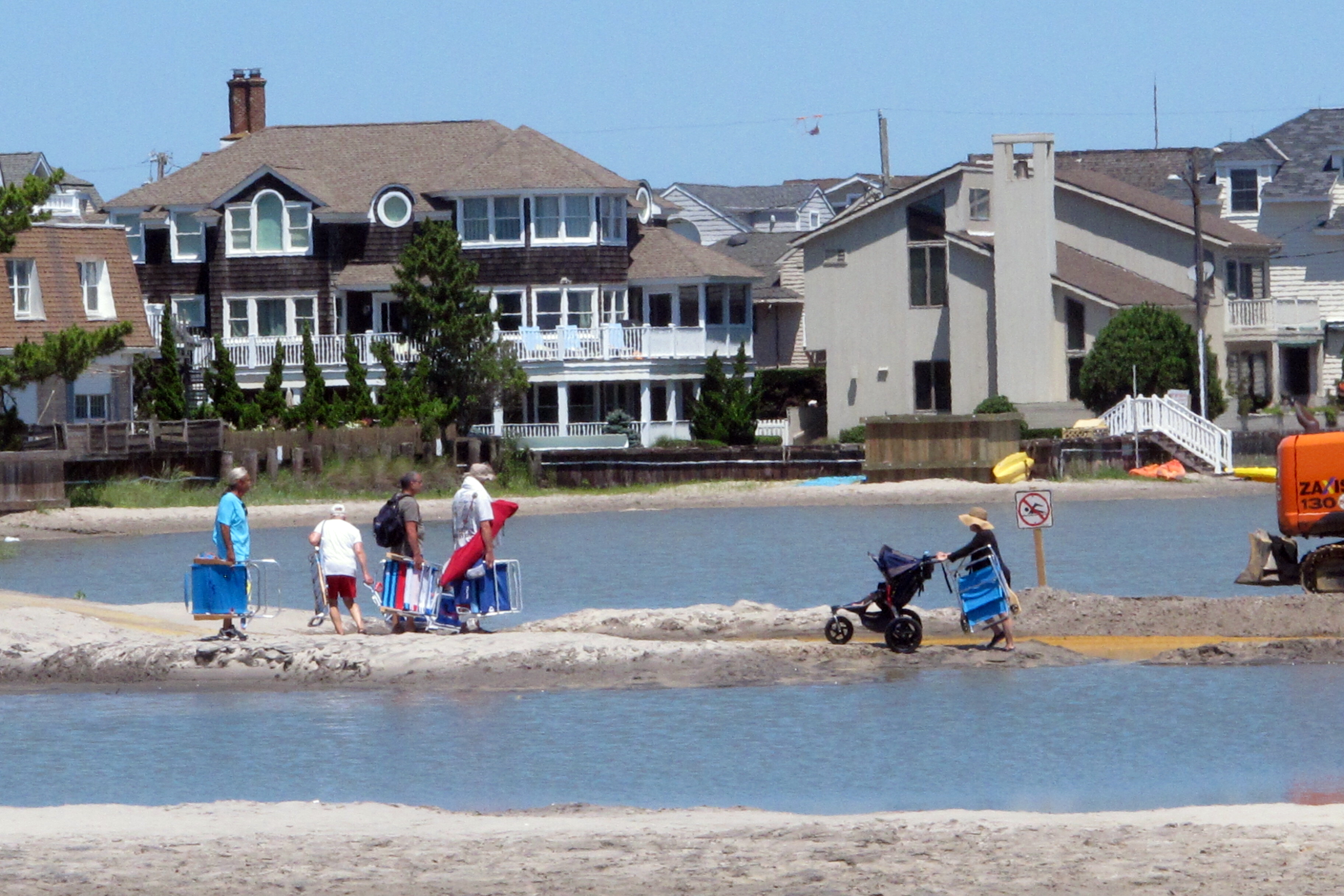 Beachgoers cross over one of numerous large pools of water that formed on the beach in Margate, N.J., after heavy rains in July 2017. The water was blocked from draining into the ocean by sand dunes built as part of a storm protection program that Margate residents vigorously fought, claiming that the dunes would cause exactly the type of standing water that occurred.