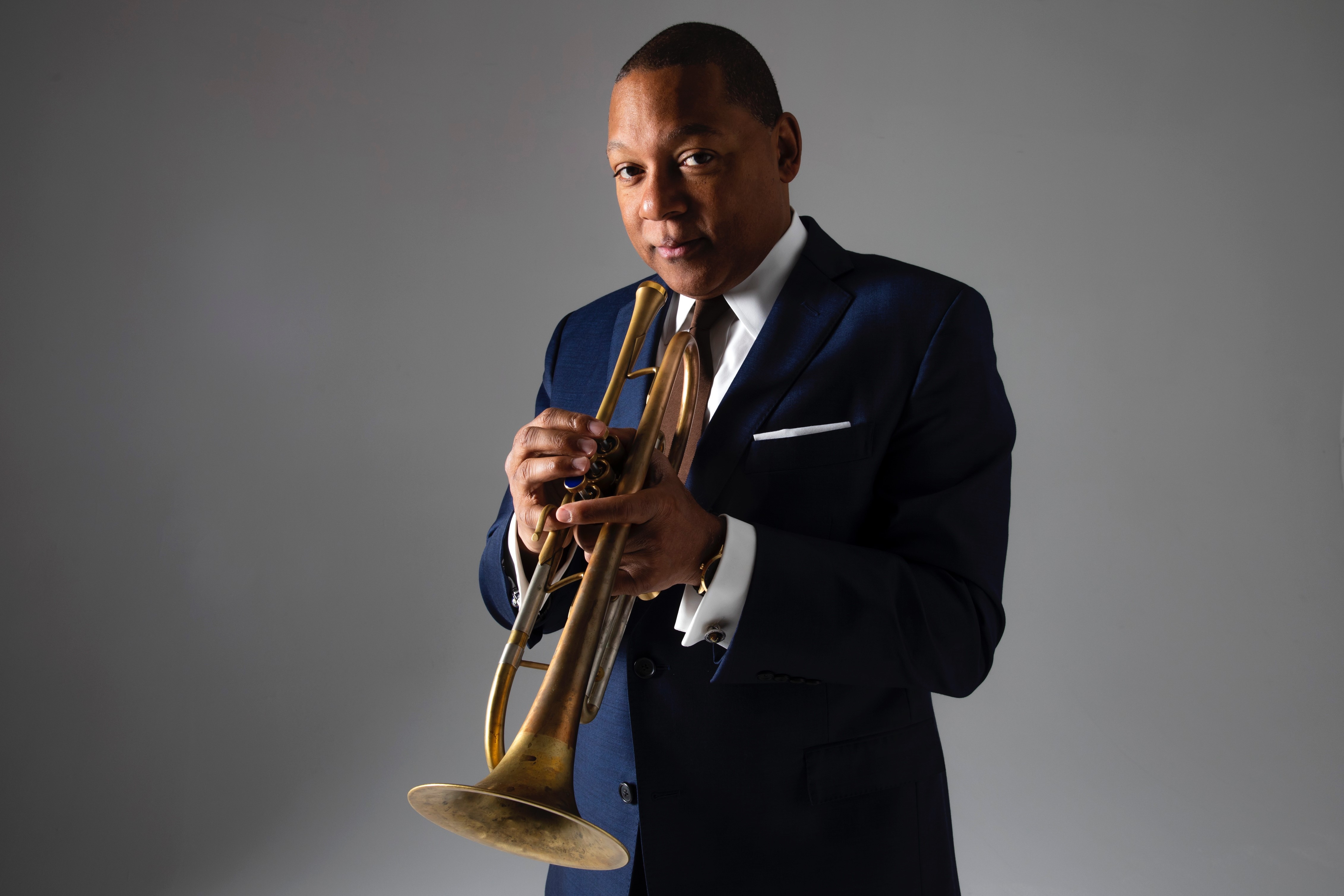 Photo of the trumpet player Wynton Marsalis holding his horn in a blue navy suit.