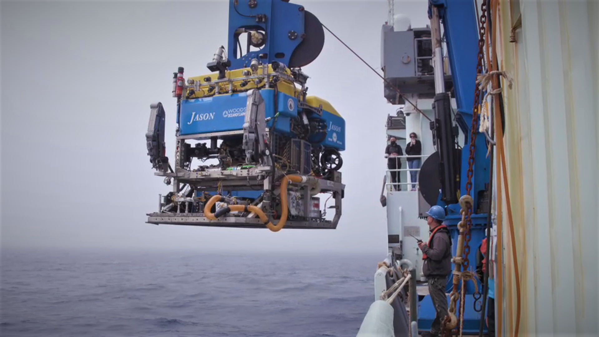a robot fit to explore the ocean is hanging by a crane on a research ship