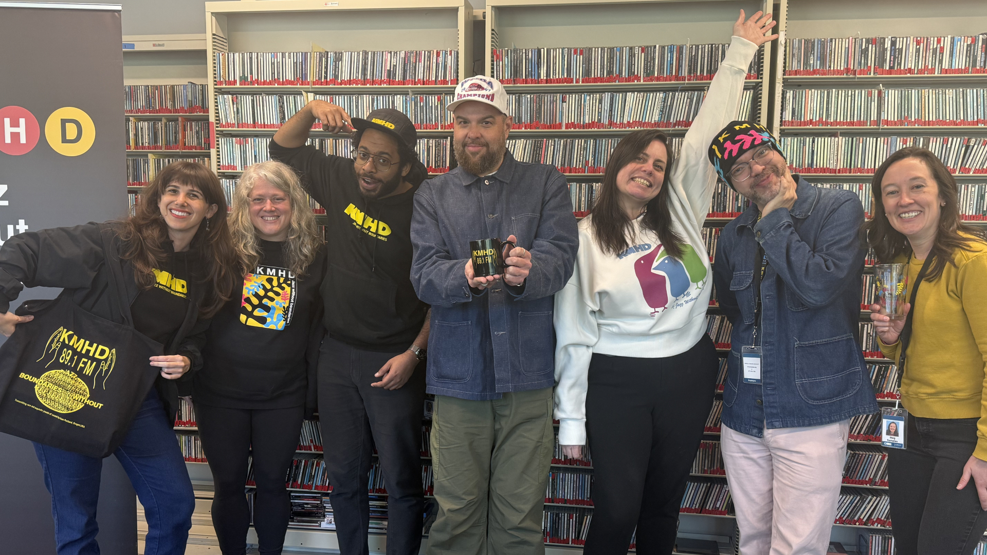 Blair Stapp with the KMHD Spiritual Jazz tote, Nicole D'Amato, Anthony Dean-Harris with the KMHD 5-panel hat, Rev Shines with the Spiritual Jazz mug, Bri Drennon with the "Tappen Trio" crew neck sweatshirt, Alex Newman with the black fern beanie, and Meg Samples with the fern pint glass (l-r).