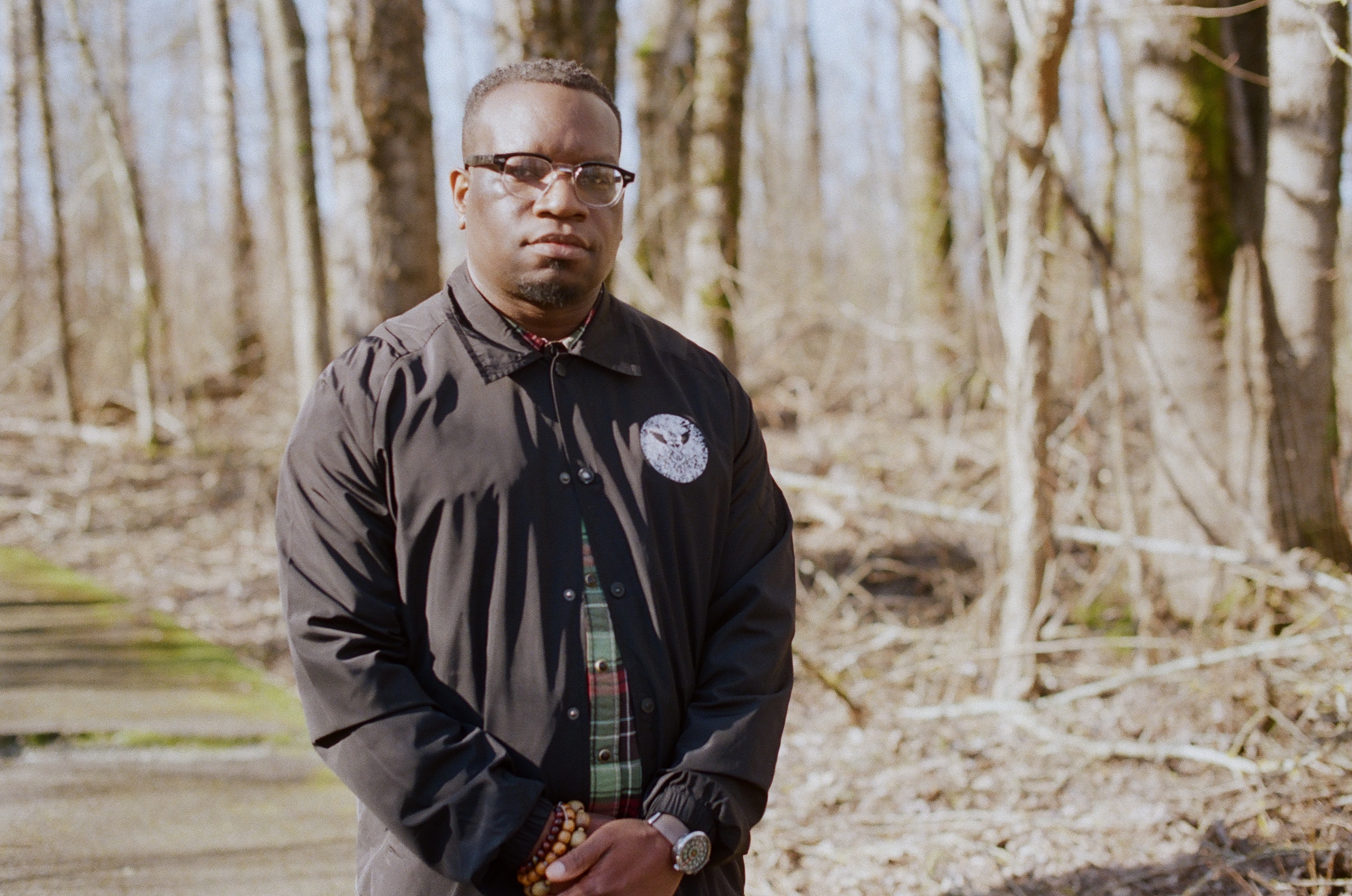 Darrell Wade stands with his held together in a wooded area. Portrait style.