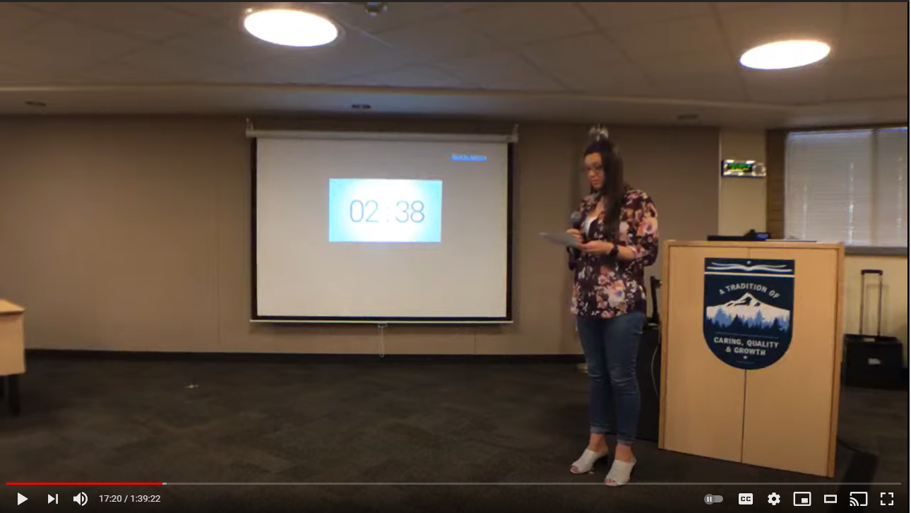 A video screen shot from a meeting's livestream feed shows an adult standing in front of a podium and speaking while not wearing a mask or other face covering.