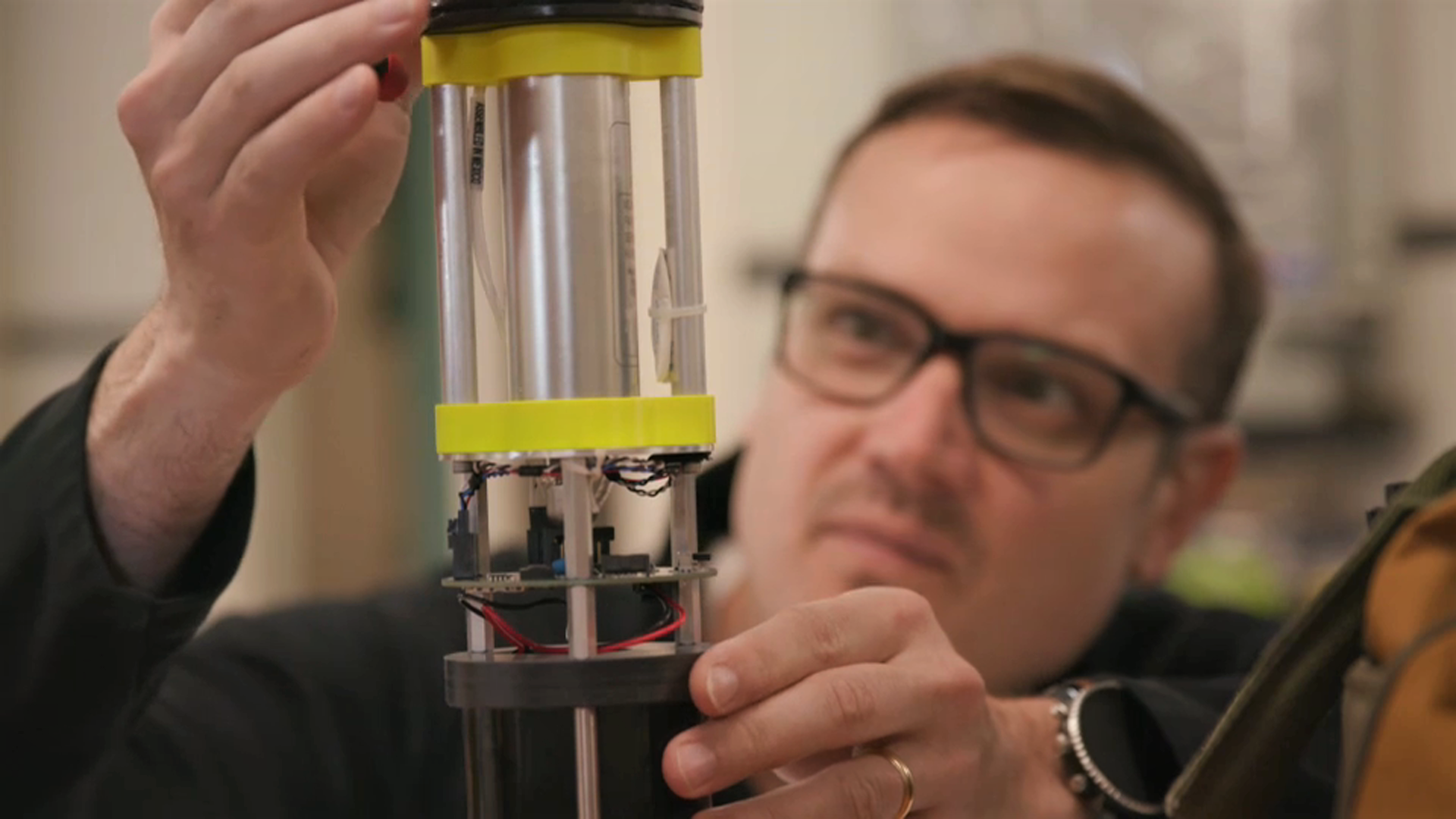 a man in glasses in the background operating a tube shapes device that collects pressure data