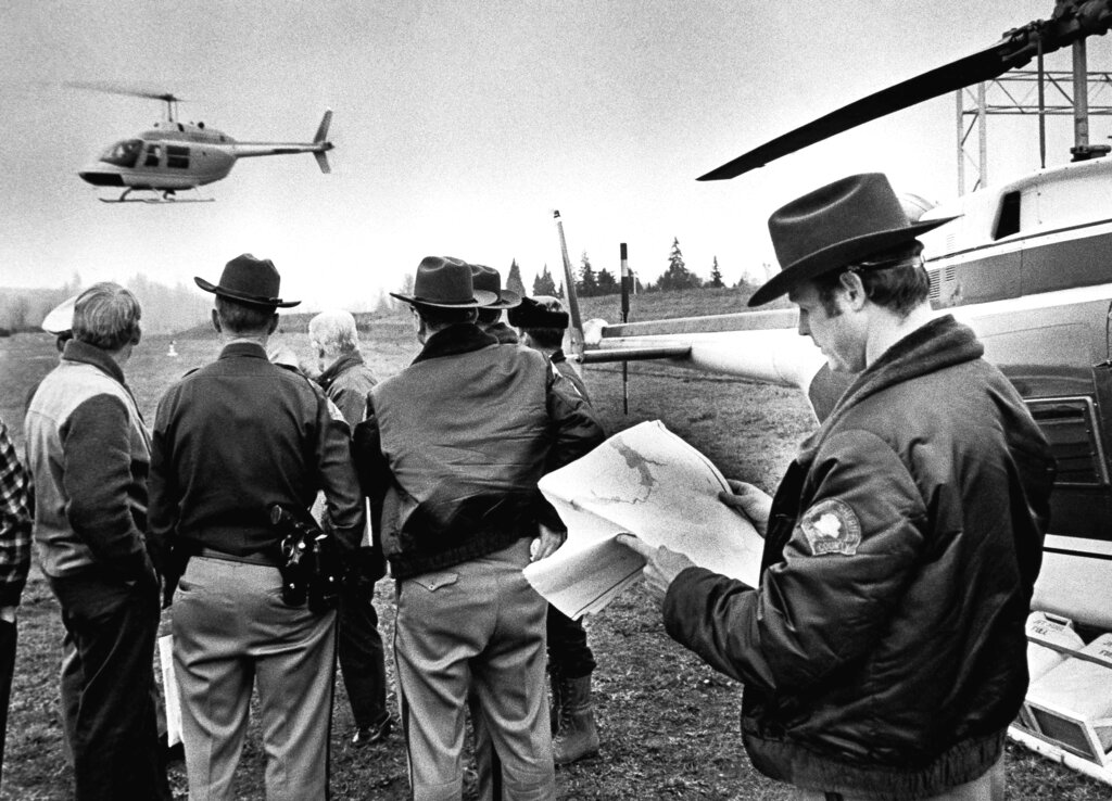 A group watches as a helicopter files low to the ground.