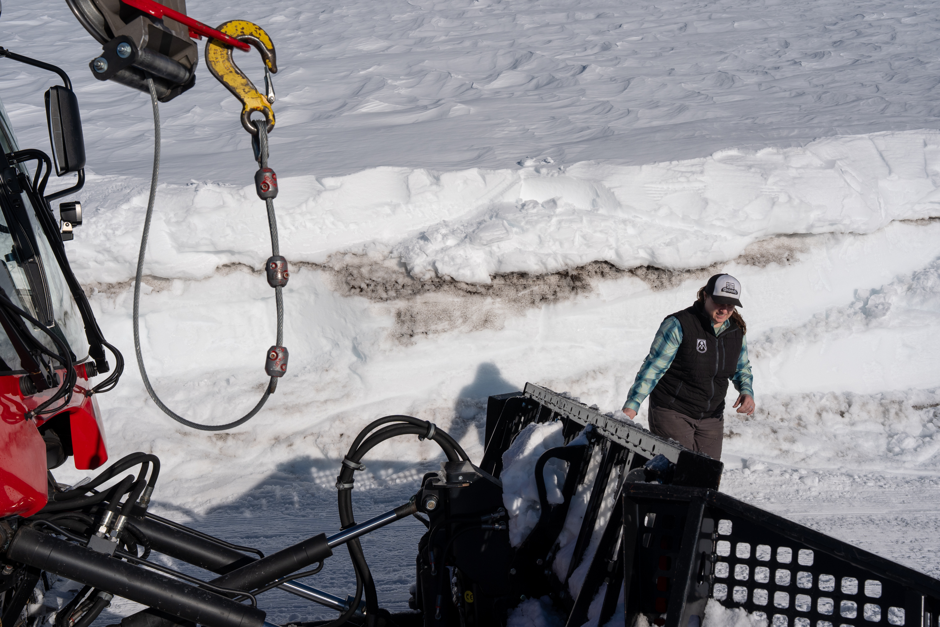 Mt. Hood Meadows grooming manager Allison Mariner checks on her snowcat while showing the snow conditions at Mt. Hood Meadows in Mt. Hood, Ore., on April 4, 2026. Layers of dirt and snow are piled up in a large drift behind Mariner due to dirt accumulation carried by wind during periods of time without new snowfall.