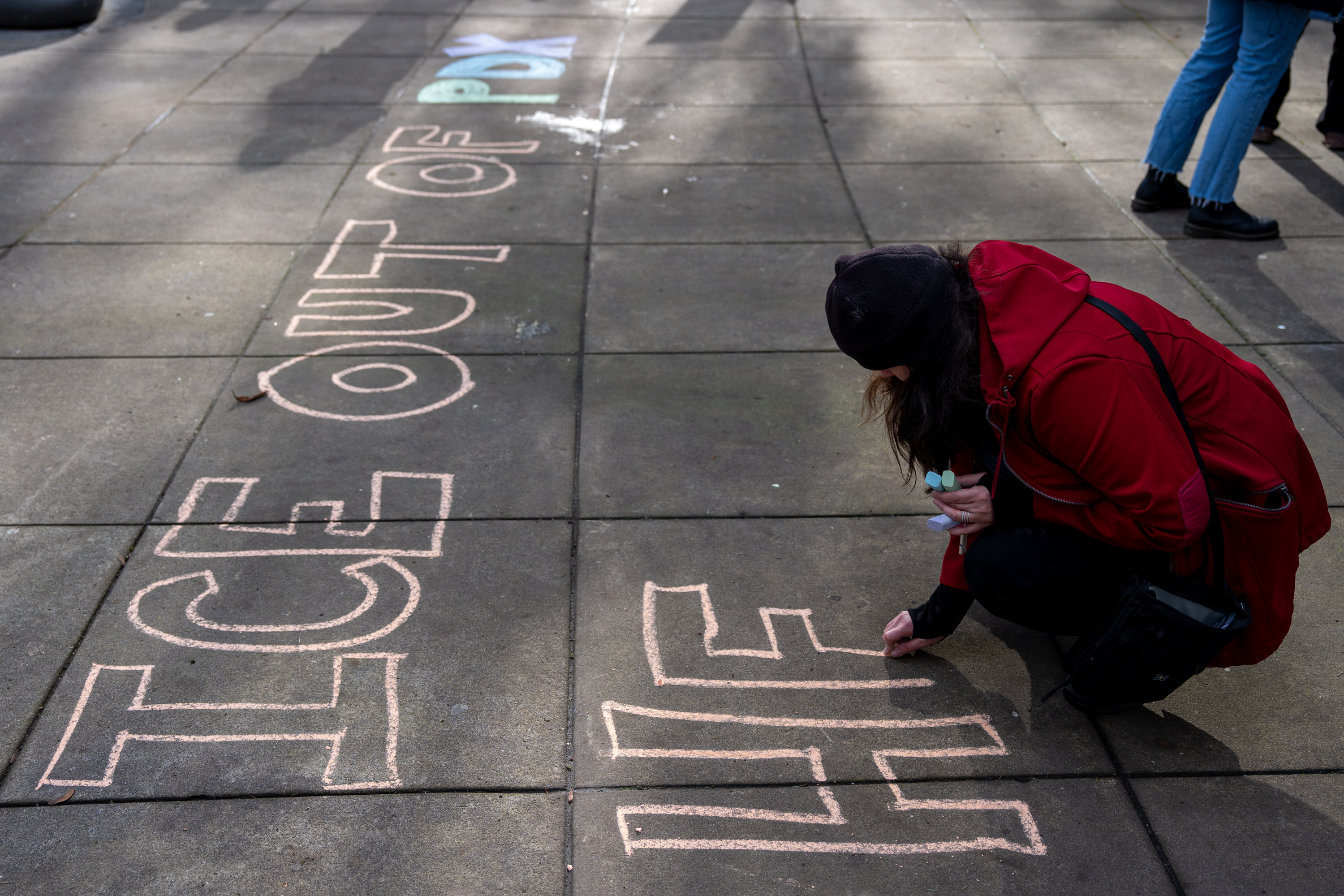 Indivisible organizer Tara Velarde writes, “ICE out of PDX health care!” during a demonstration at Dawson Park, across the street from Legacy Emanuel Medical Center, in protest of the hospital working with ICE to treat detainees they harm during arrests in Portland, Ore., on Jan. 10, 2026.