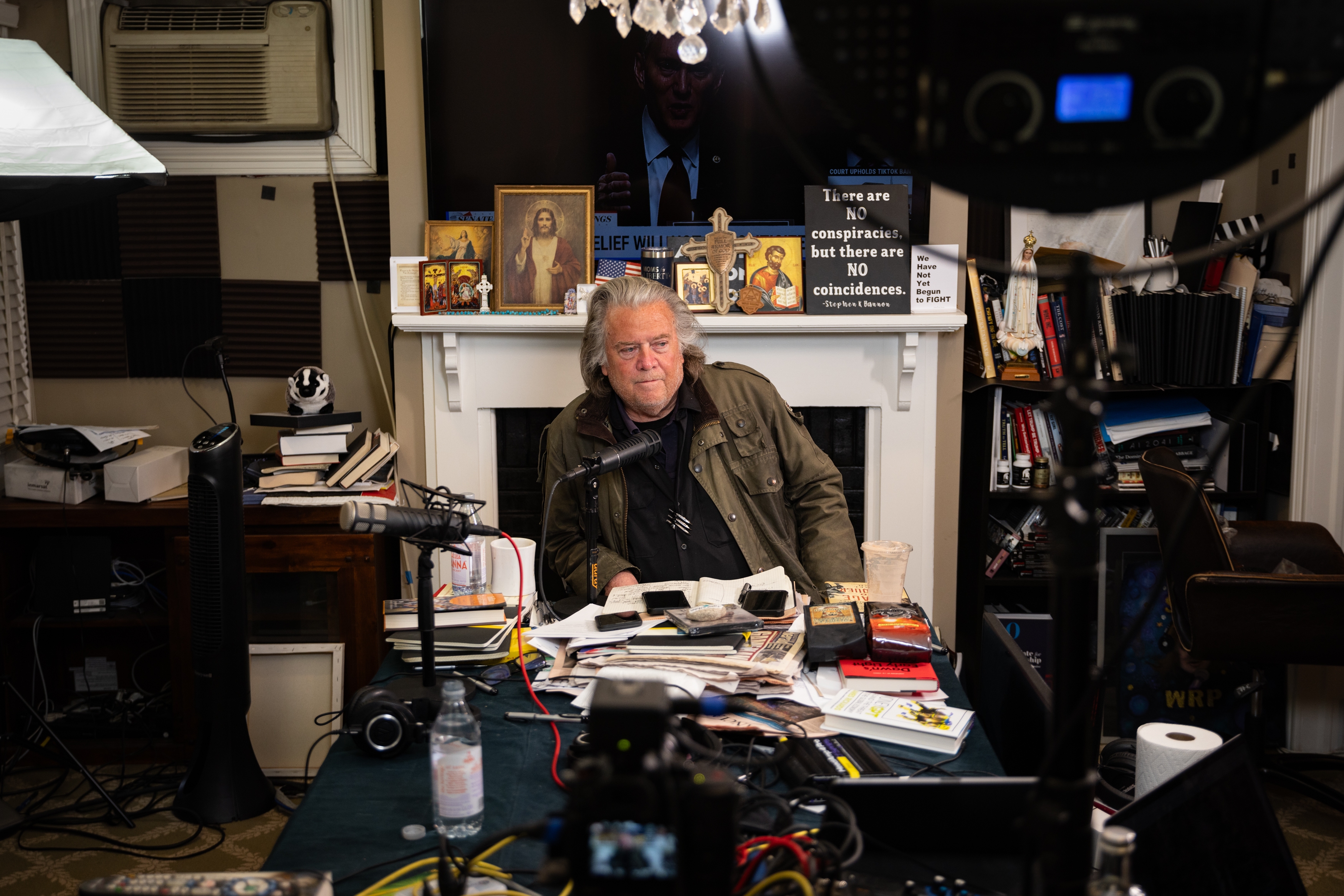 Bannon broadcasts in front of a fireplace mantel decorated with paintings of Jesus Christ, crosses and signs.