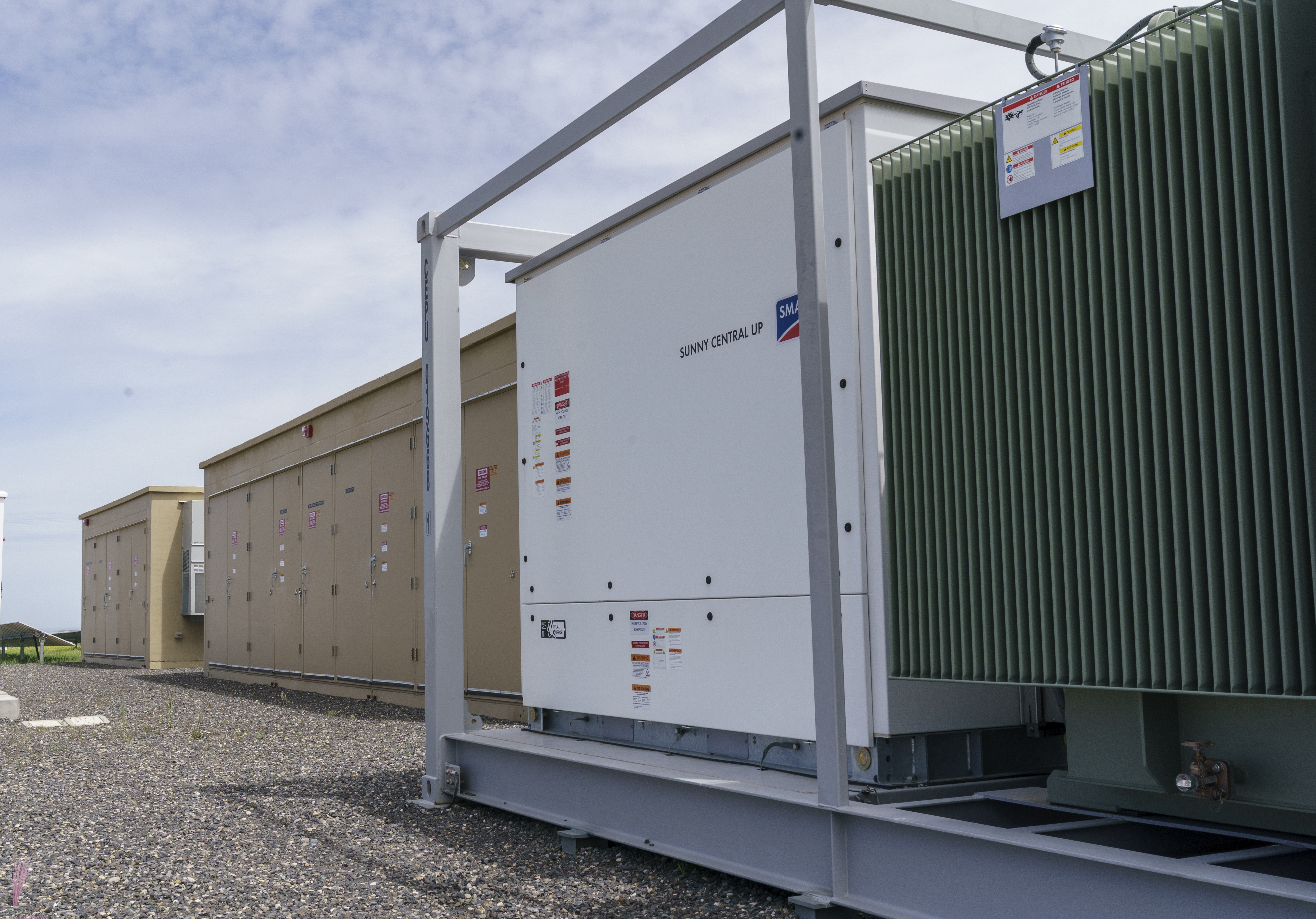 Power generated by solar panels passes through an inverter, right, is converted to alternating current, and then carried to batteries, left, housed on site.