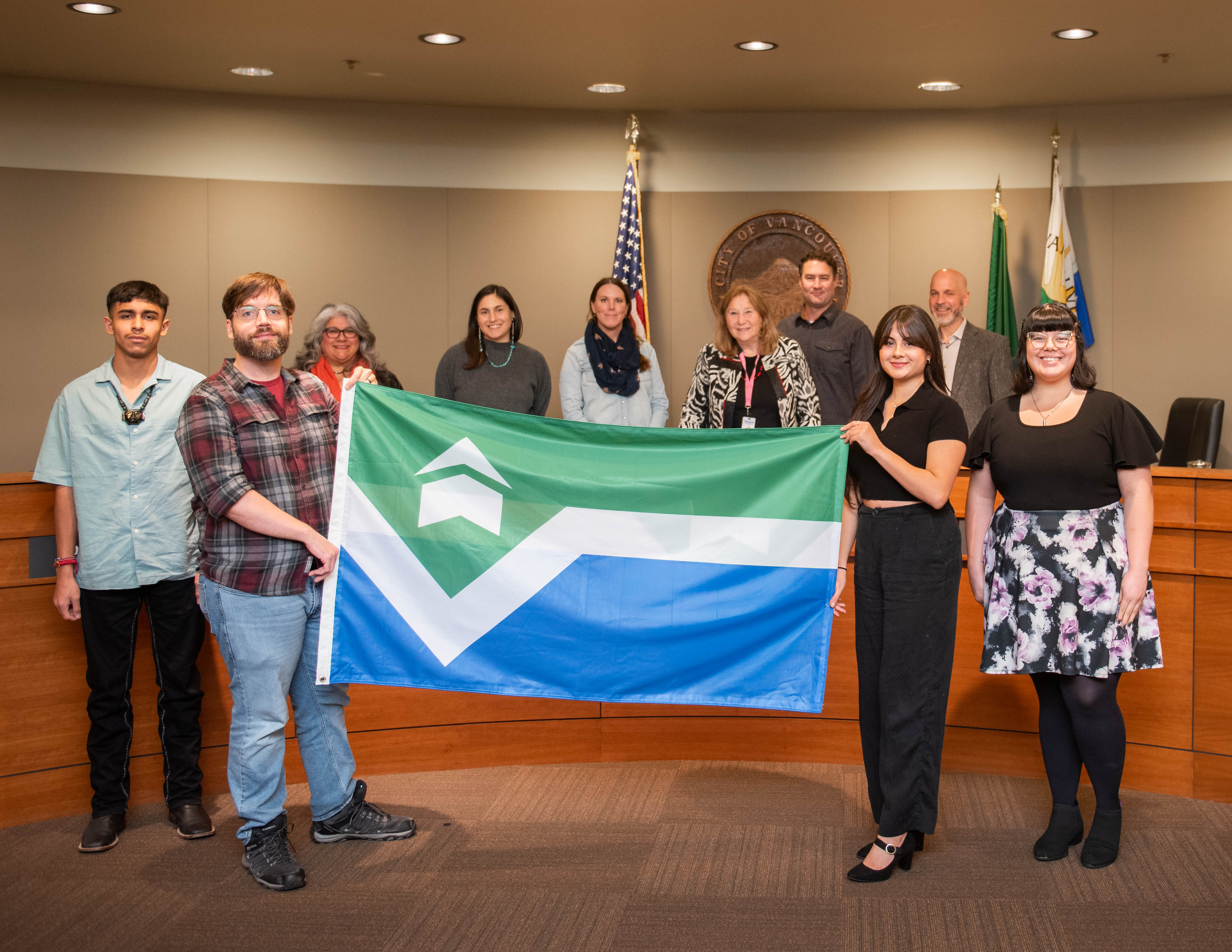 Nathan Hunter, second from left on the front row, and Brooke Nugent, second from right on the front row, hold the flag they designed at a city council meeting in Vancouver, Wash., on Nov. 10, 2025. Front row: Flag Selection Committee Vice Chair Hèctor Alejandro Varela-Betancourt, left, and Chair Rose Mendoza, right. Back row from left to right: Councilmembers Diana Perez, Kim Harless and Sarah Fox; Mayor Anne McEnerny-Ogle; and Councilmembers Bart Hansen and Ty Stober.