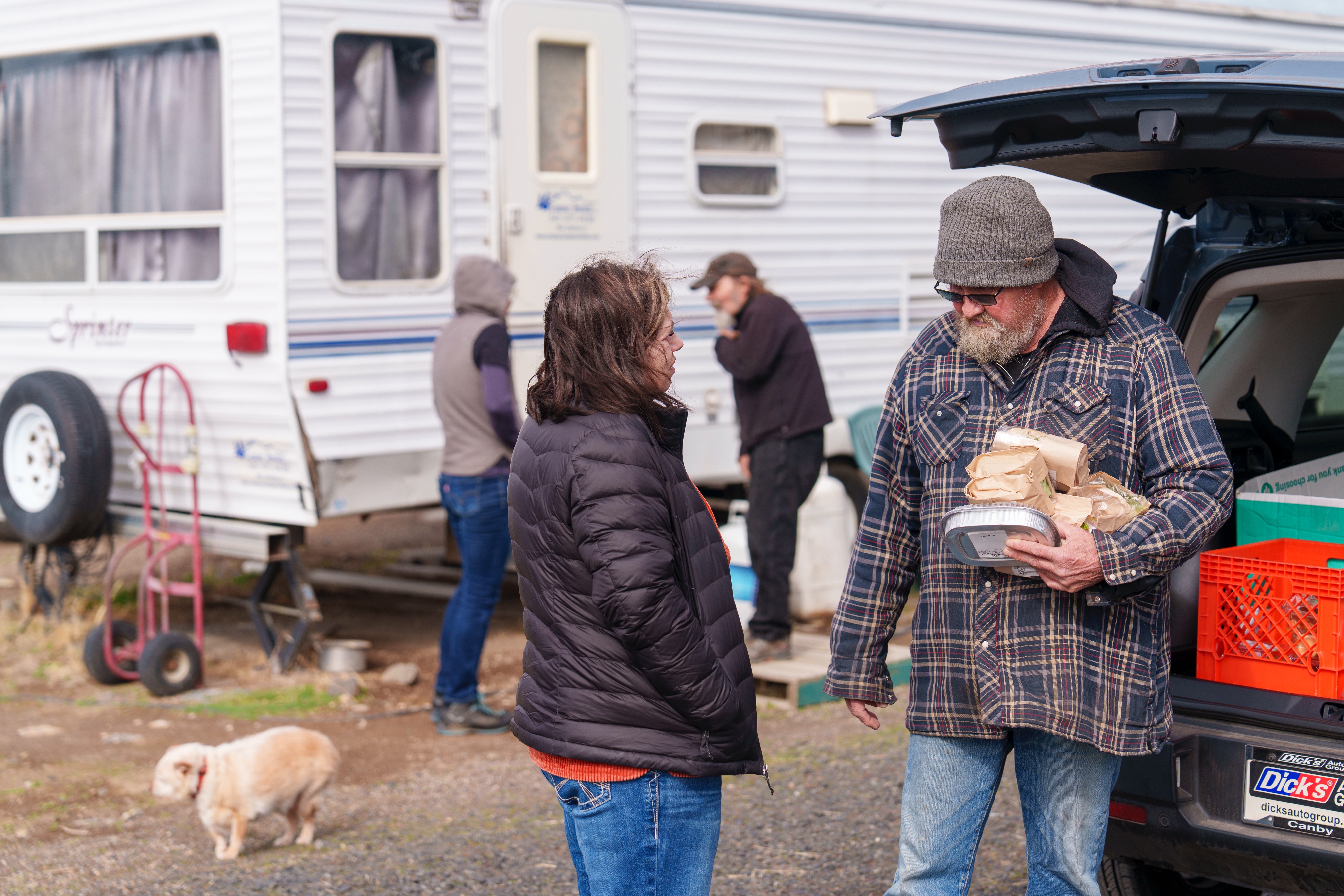In a photo provided by Mountain View Community Development, case manager Stephanie Buechert (left) delivers food and talks with Don, a former participant at a safe parking site in Redmond, Ore., in March 2025.