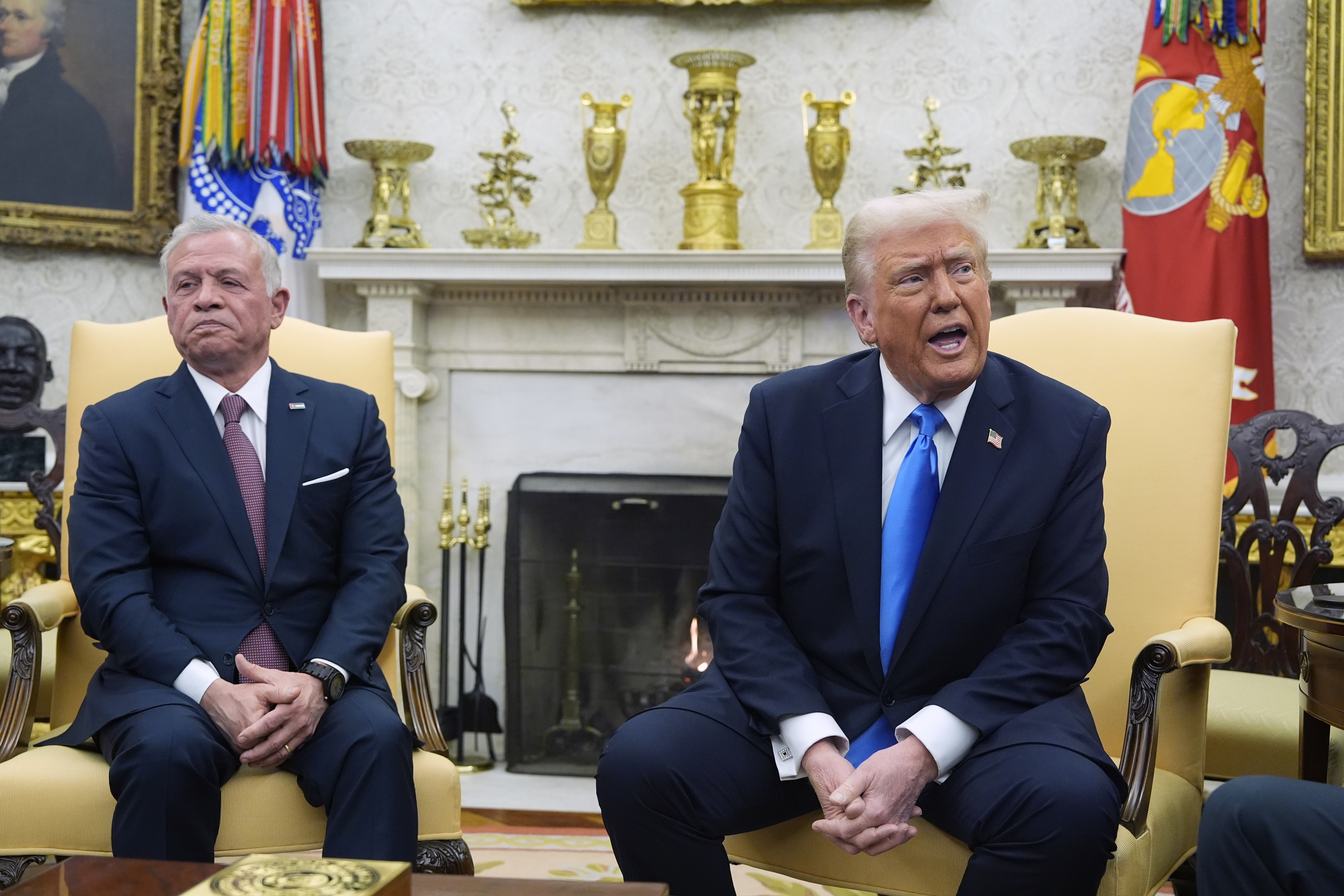 In this photo, President Trump and Jordanian King Abdullah II sit on armchairs at the White House. Both are wearing dark blue suits, and Abdullah II is on the left, while Trump is on the right. A fireplace is behind them.