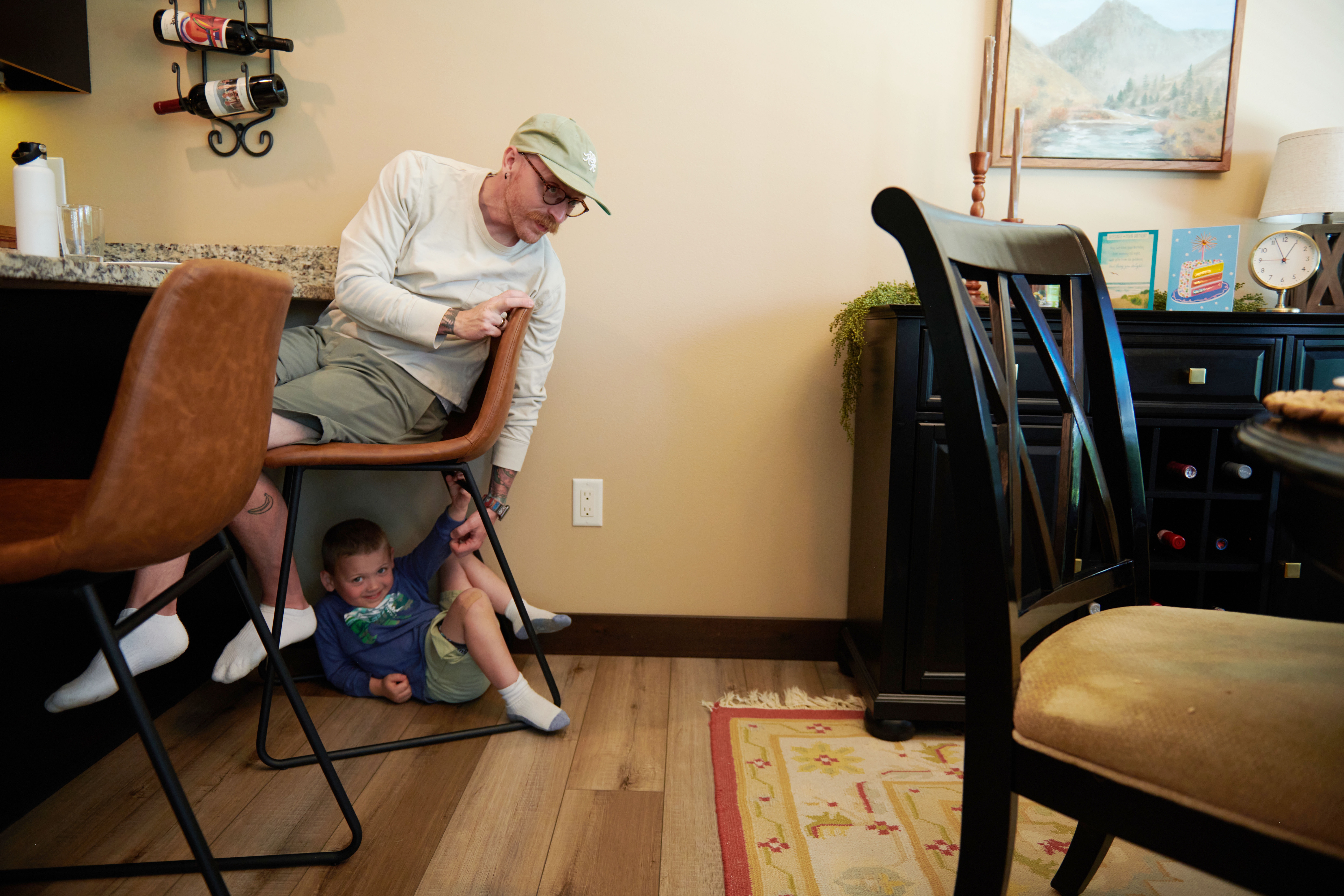 Neil Petersen sits in a chair as Jack, 4, plays underneath him.