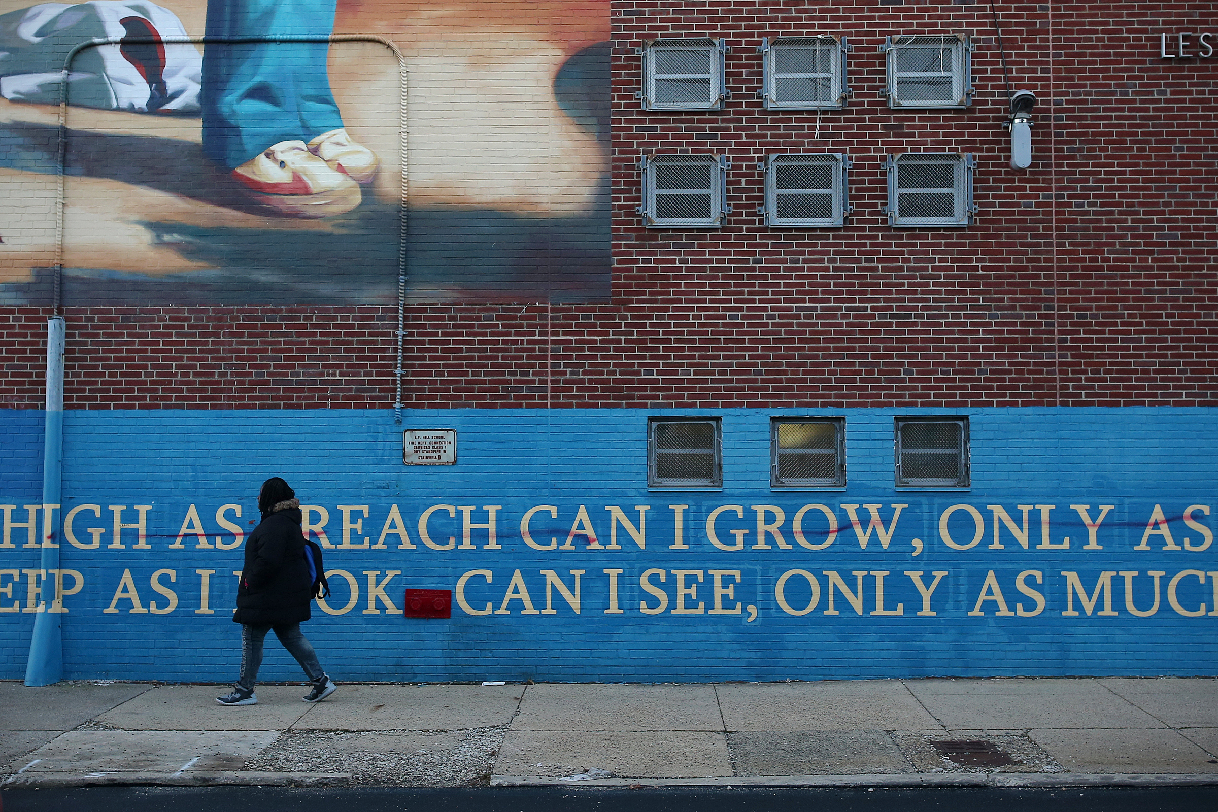 Strawberry Mansion senior Charnel Crockton passes a mural on the now-closed Leslie P. Hill School building as she walks from a nearby bus stop to Strawberry Mansion High School. Crockton takes two buses to get to school each morning from the Germantown youth shelter where she lives.