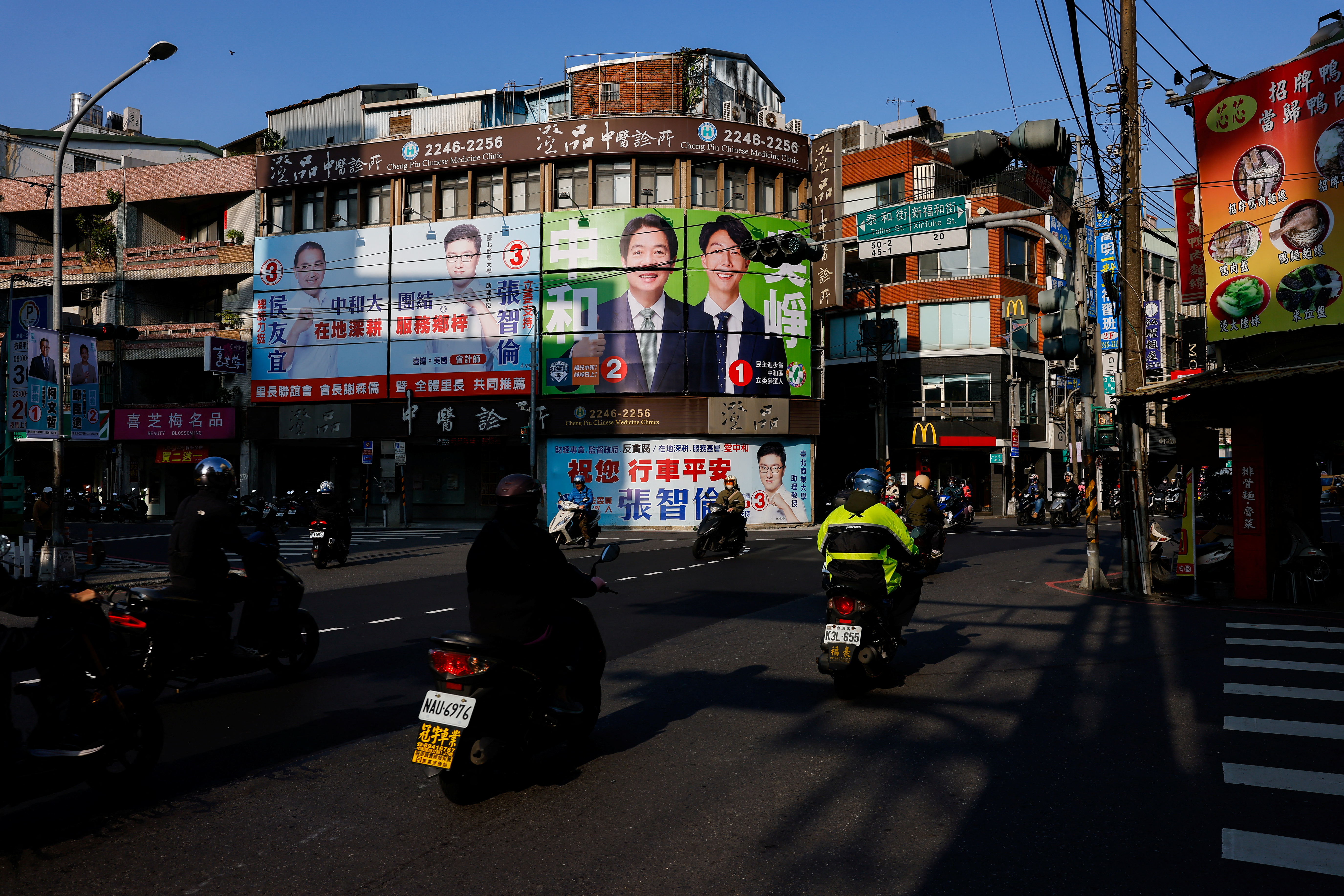 People ride past campaign ads for presidential and parliamentary candidates in ahead of the general election in Taipei, Jan. 12, 2024.