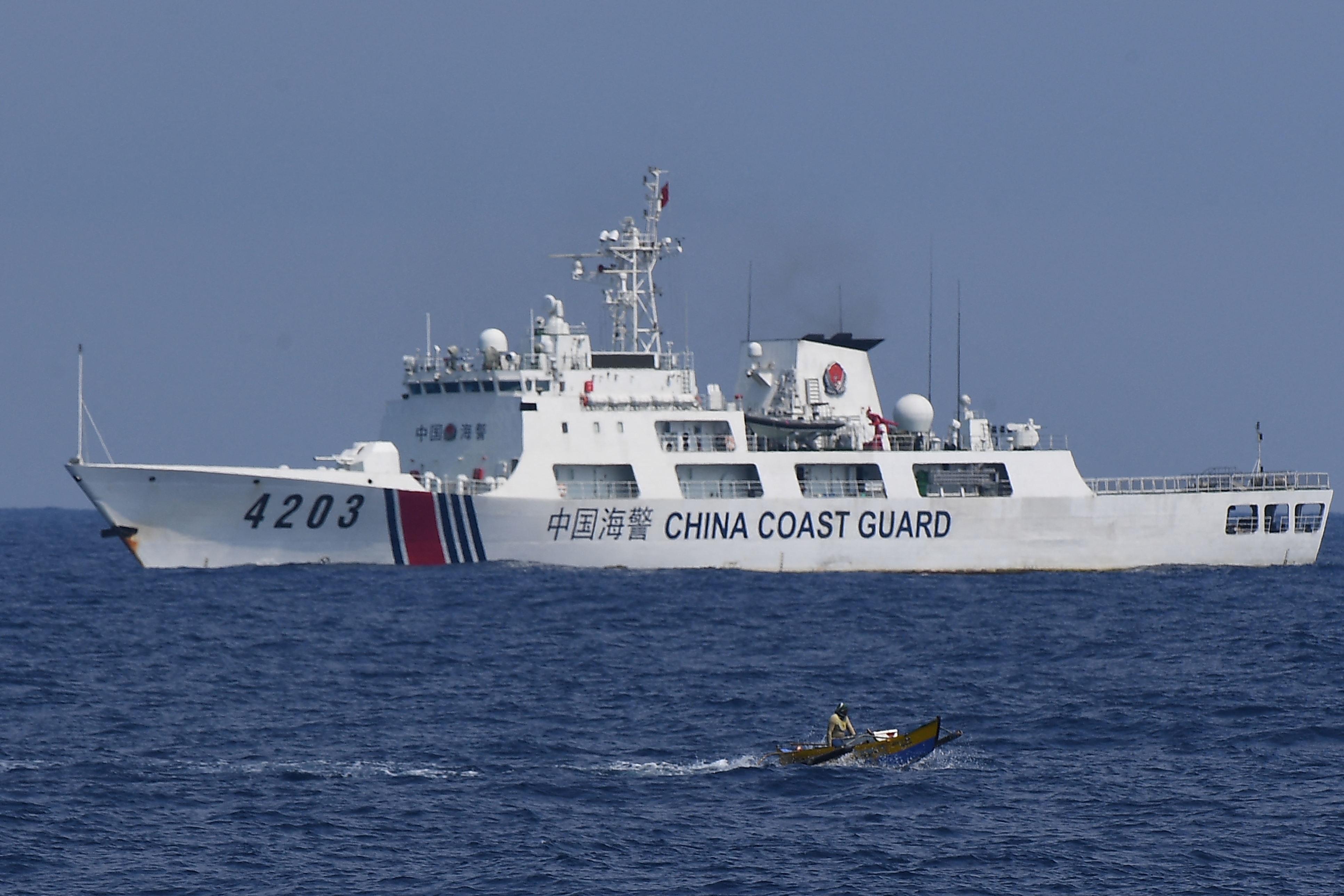 A China Coast Guard ship monitors a Philippine fisherman aboard his wooden boat in the disputed South China Sea, May 16, 2024.