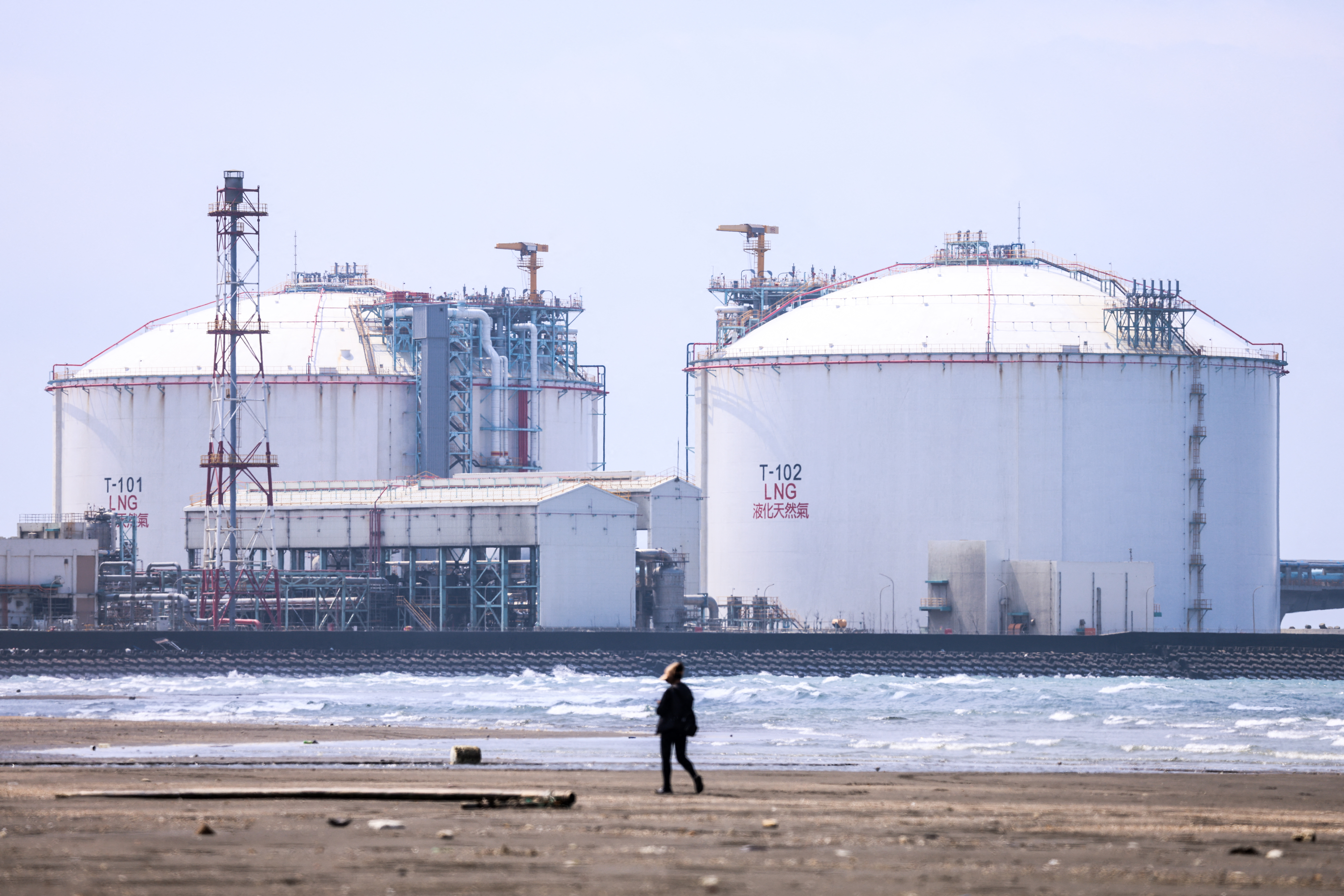 A tourist walks on a beach with the background of Guan-Tang LNG Receiving Terminal, a major liquefied natural gas import facility in Taiwan, March 25, 2026.