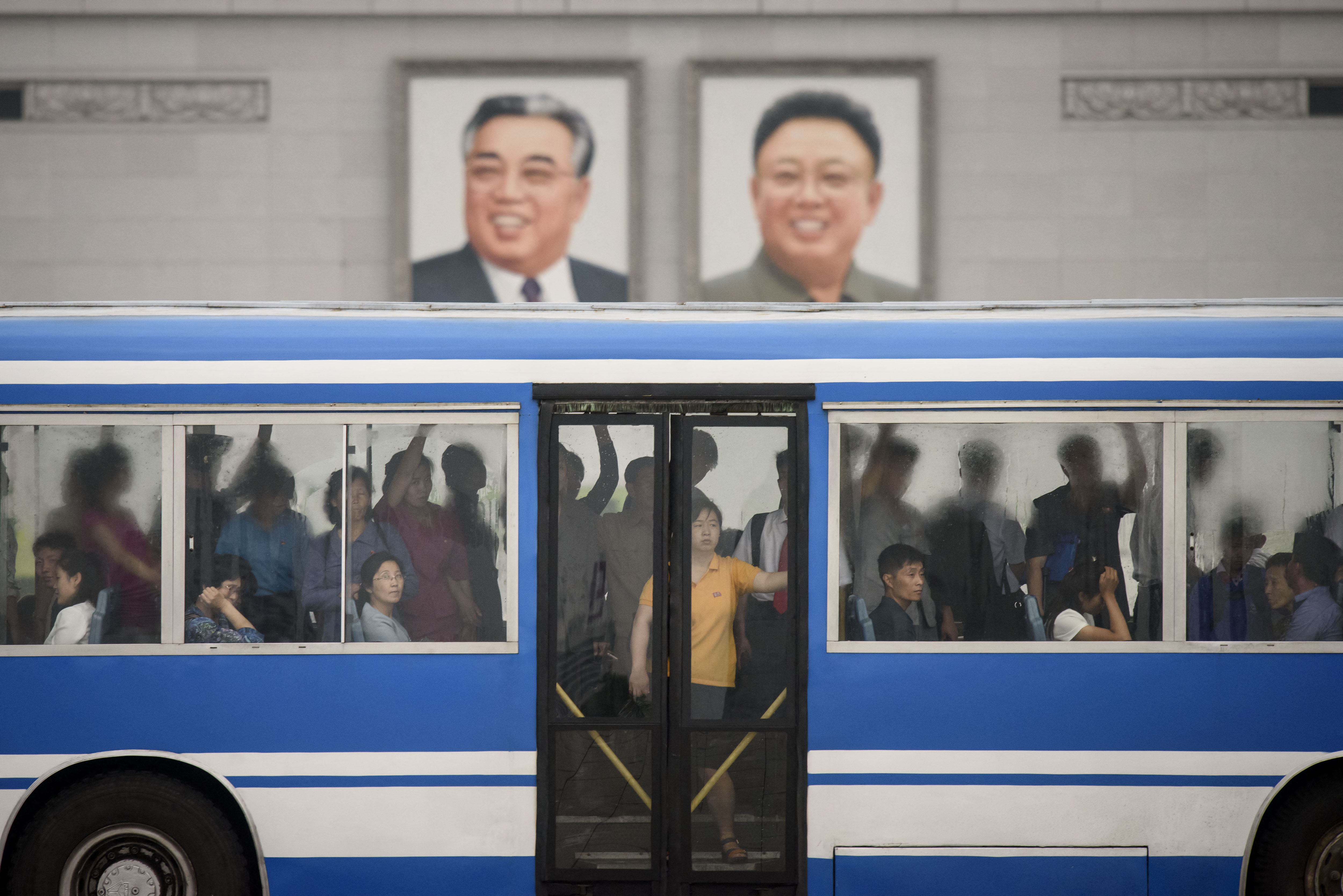 2019년 6월 18일, 평양 김일성 광장에서 통근자들이 버스를 타고 김일성, 김정일 등 북한 전 지도자들의 초상화 앞을 지나가고 있다.