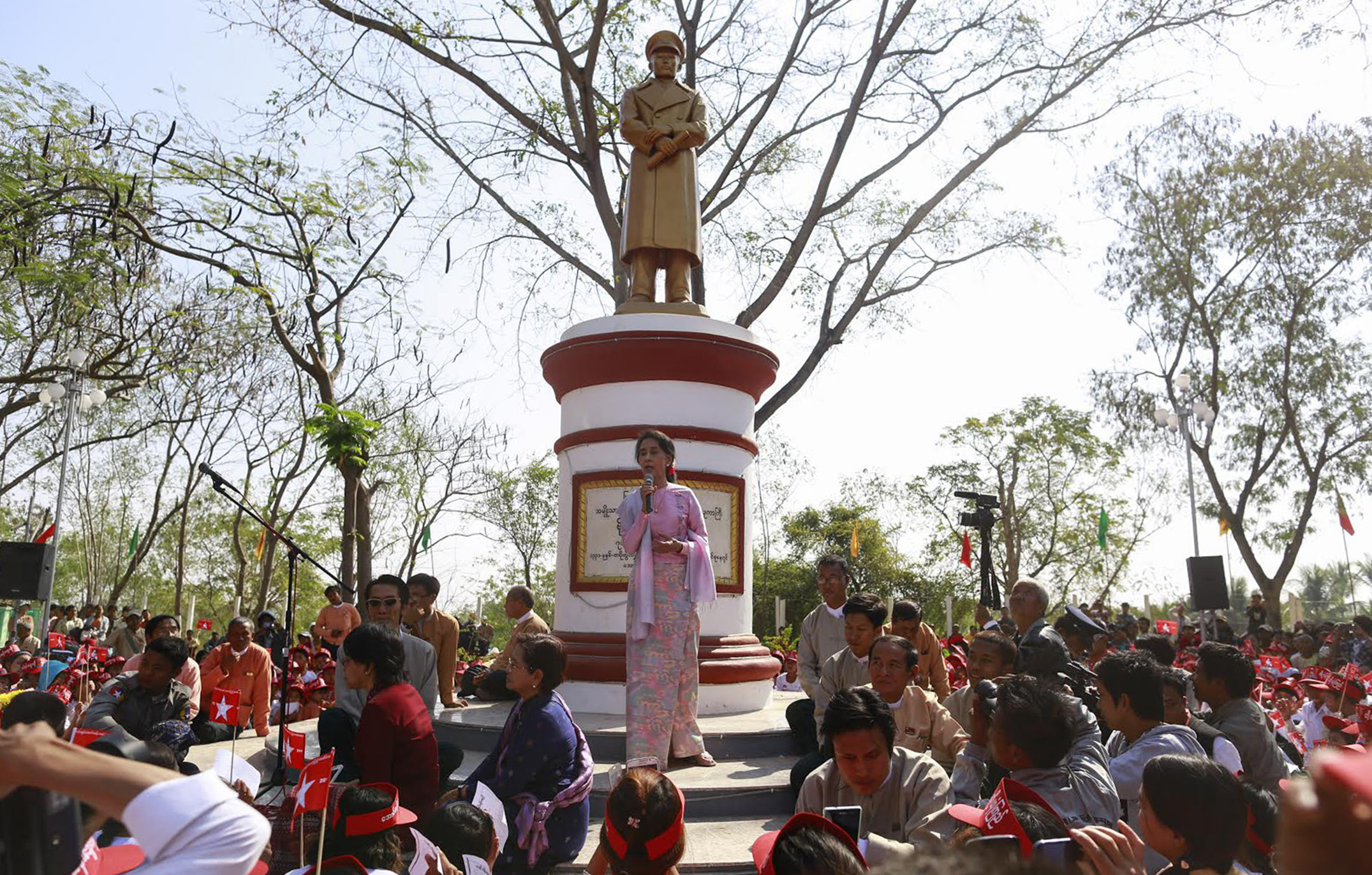 A Feb. 13, 2015, photo shows Aung San Suu Kyi speaking in front of a statue of her father General Aung San to mark his 100th birthday anniversary in his hometown of Natmauk, in Magway district of central Myanmar. This statue was not among those removed.