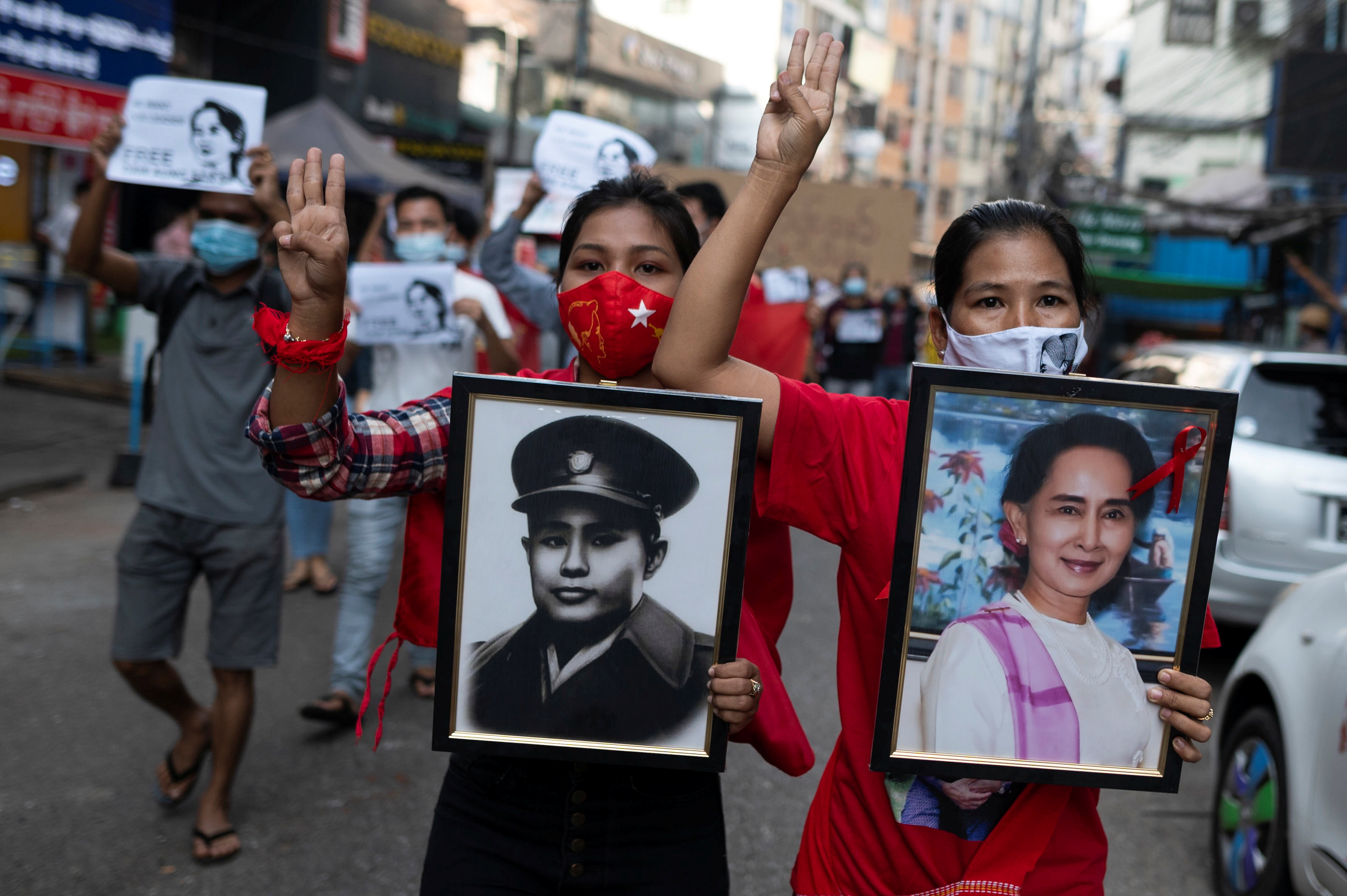 Women show the three-finger salute as they carry portraits of Aung San Suu Kyi and her father, general Aung San, during a protest against the military coup and to demand the release of elected leader Suu Kyi, in Yangon, Feb. 7, 2021.