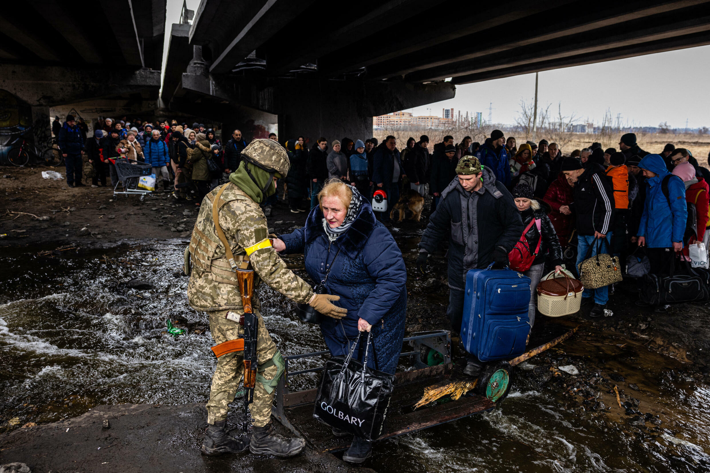 Un militar ucraniano ayuda a los evacuados reunidos bajo un puente destruido, mientras huyen de la ciudad de Irpin, al noroeste de Kiev, el 7 de marzo de 2022. - 