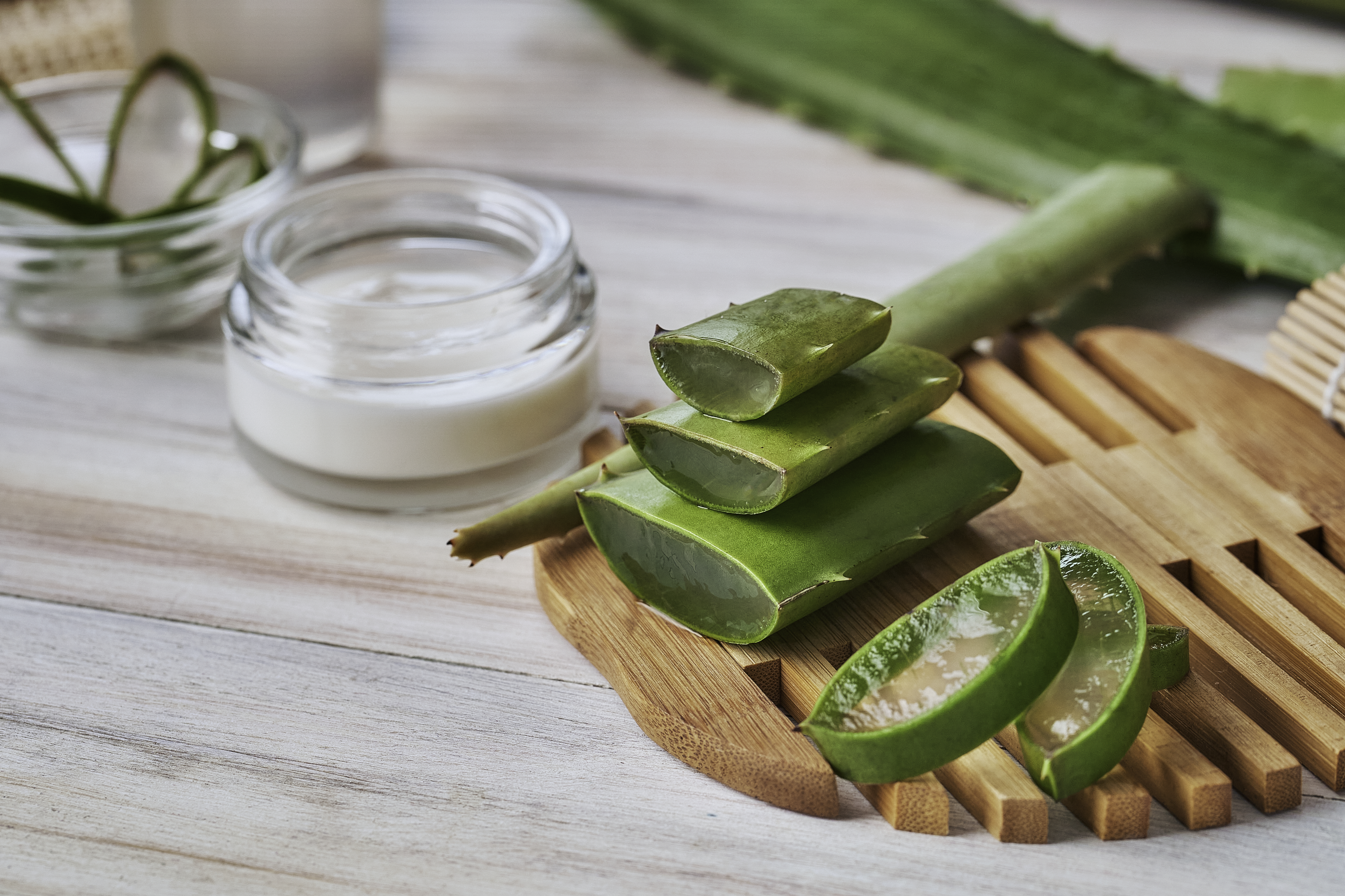 Aloe vera slices and moisturizer on a wooden table. Beauty treatment concepts