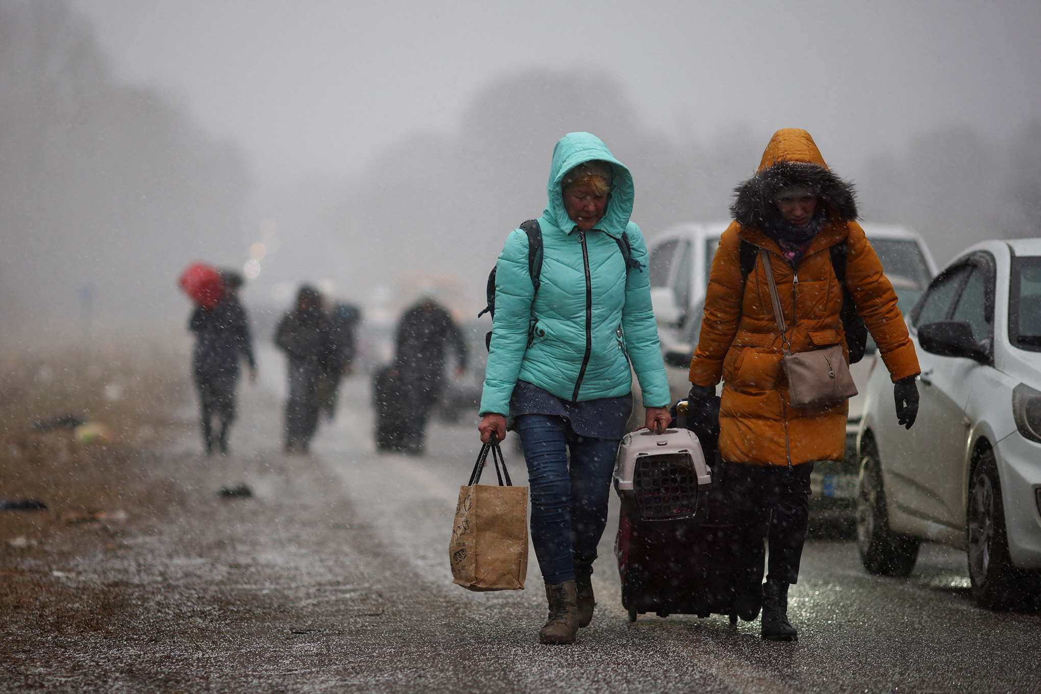 Las personas que huyen de la operación militar de Rusia contra Ucrania caminan hacia el cruce fronterizo de Shehyni a Polonia pasando los autos que esperan en fila para cruzar la frontera, en las afueras de Mostyska, Ucrania, el 27 de febrero de 2022. Foto REUTERS/Thomas Peter 