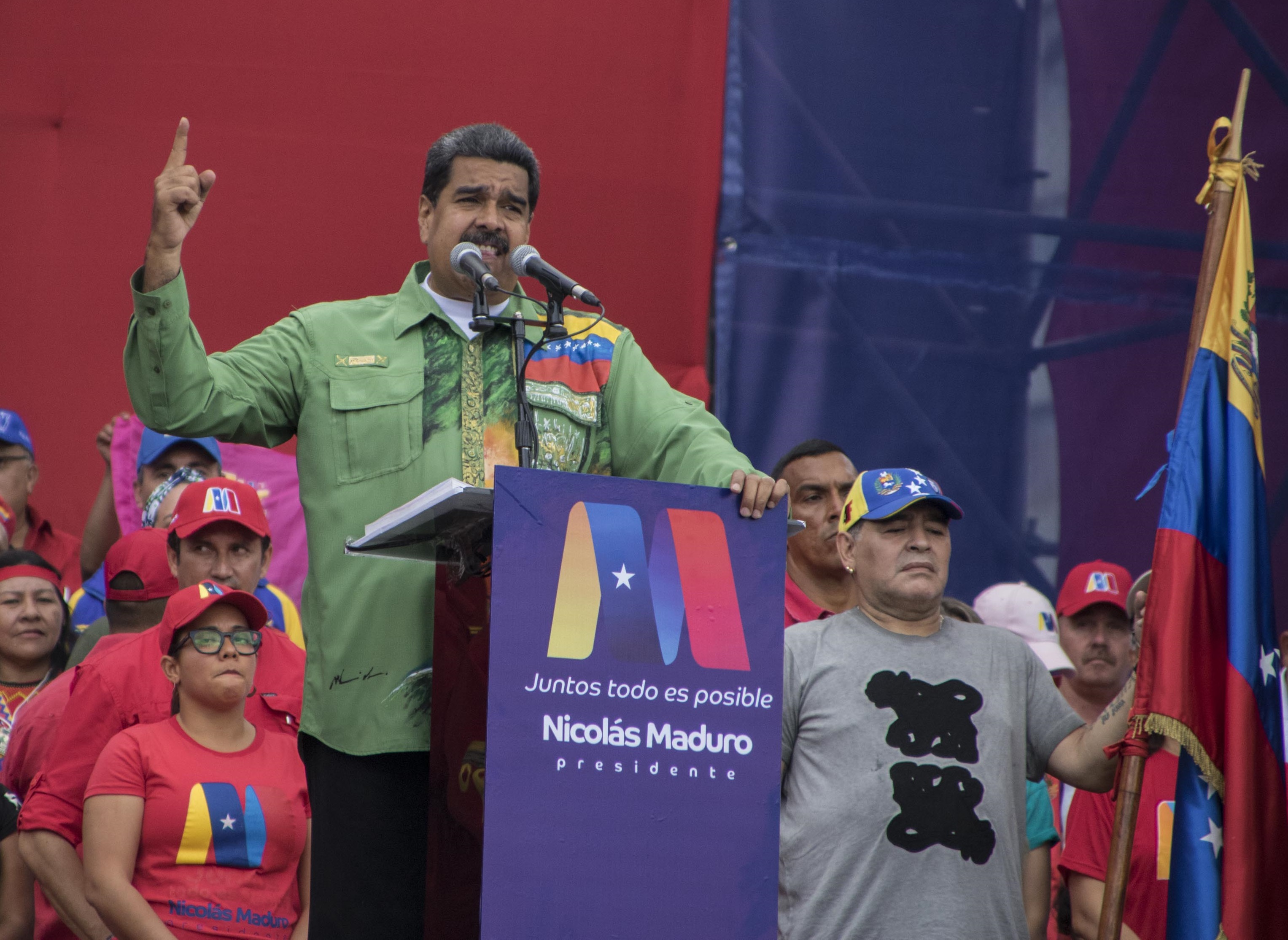 la ex estrella del fútbol argentino Diego Maradona (R) sostiene la bandera venezolana mientras el presidente venezolano, Nicolás Maduro, pronuncia su último discurso de campaña.