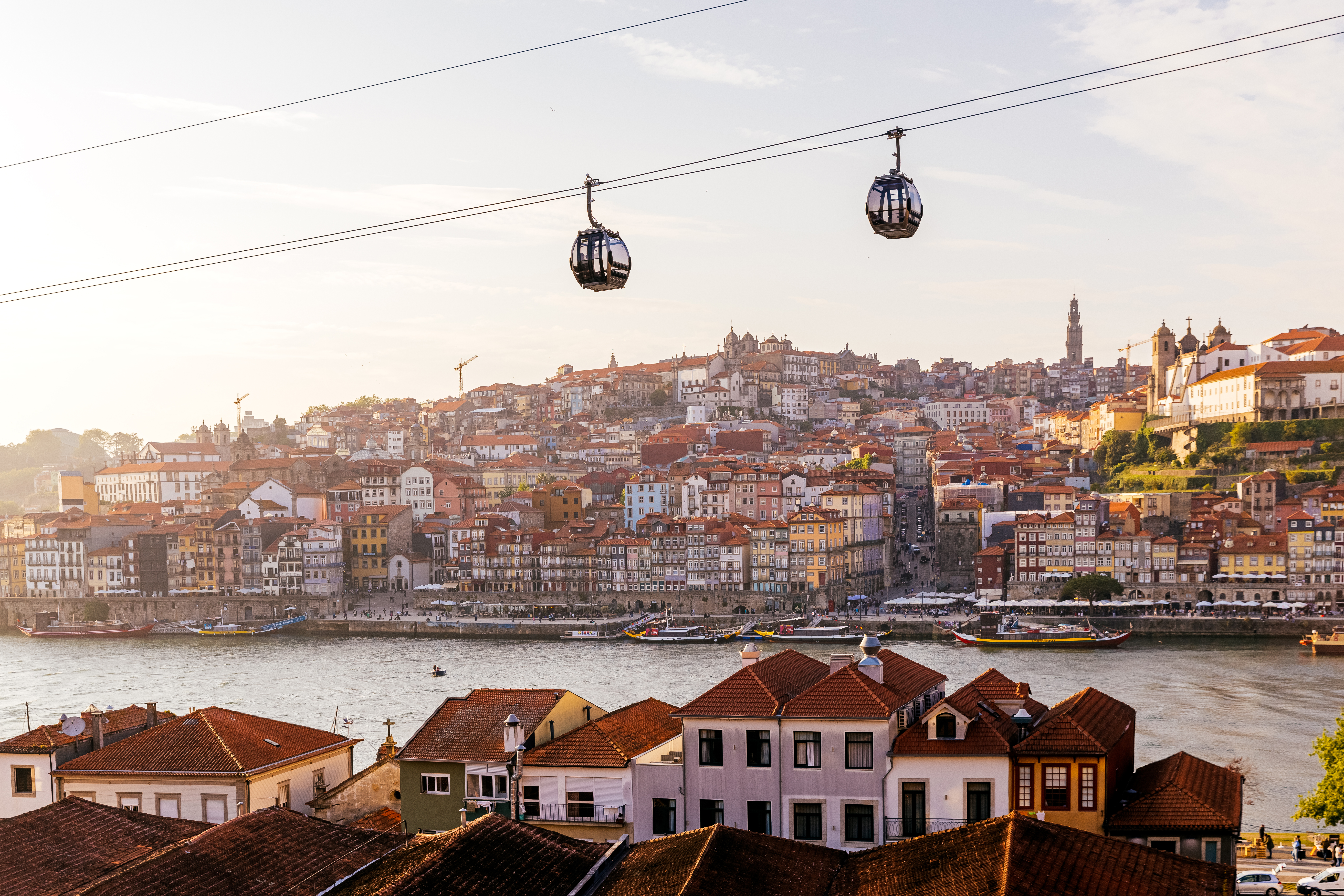 Cabinas de teleférico moviéndose sobre la ciudad de Oporto y el río Duero al atardecer, Portugal