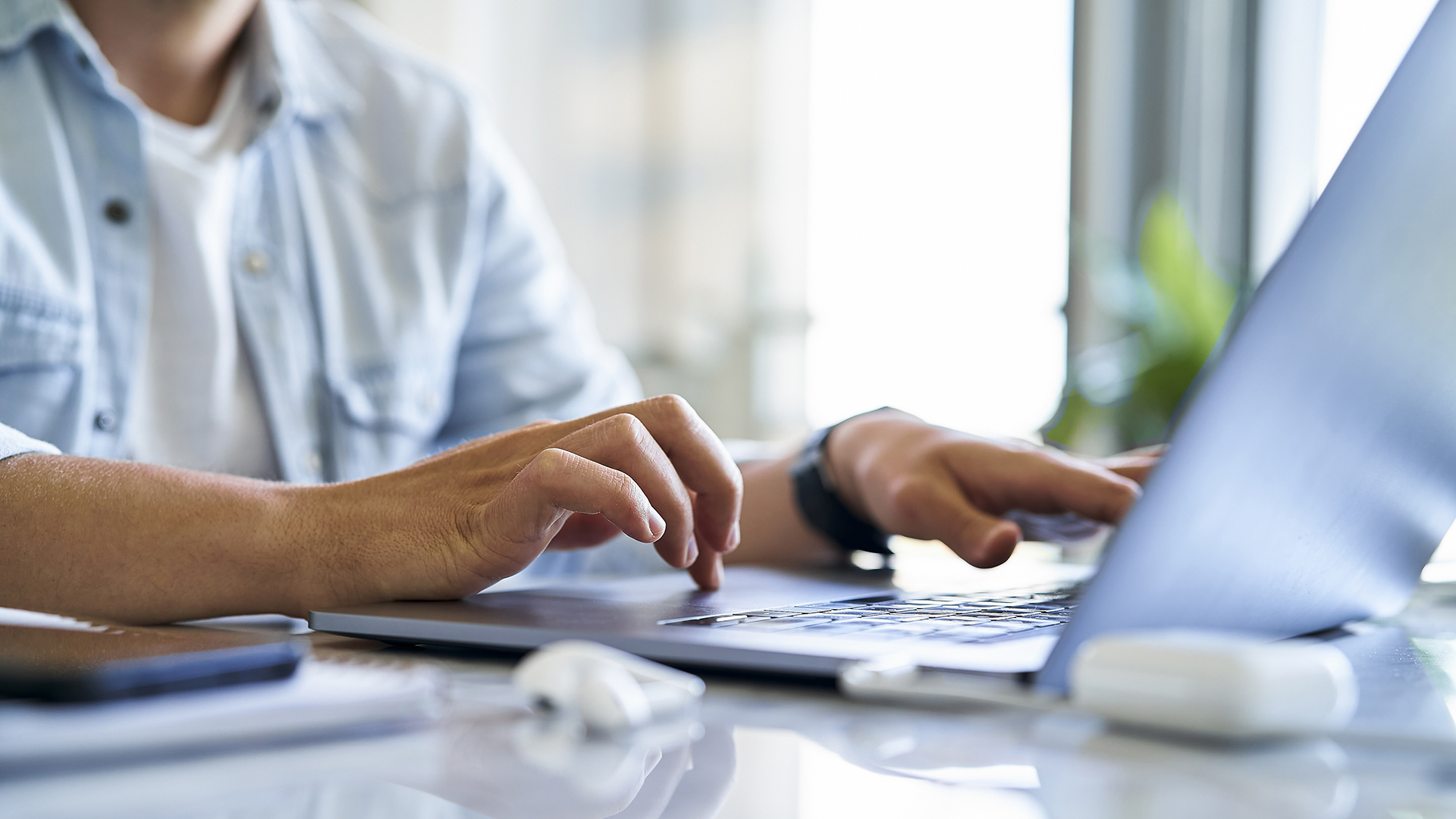 Sección media de un joven escribiendo y usando una computadora portátil mientras está sentado en la mesa en la oficina