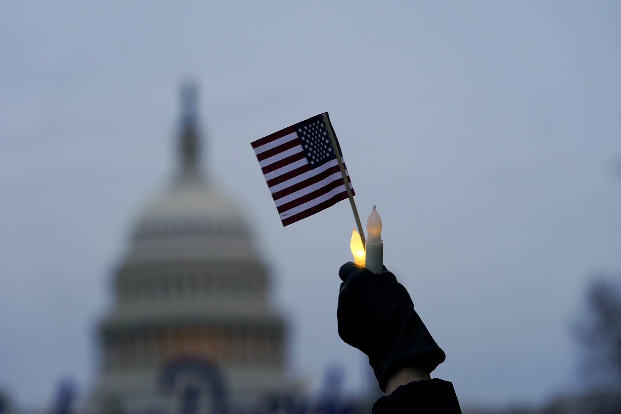 Con el edificio del Capitolio de los Estados Unidos al fondo, una persona sostiene una bandera estadounidense y velas sin llama durante una vigilia el jueves 6 de enero de 2022 en Washington, en el primer aniversario del ataque al Capitolio de los Estados Unidos. Foto AP / Julio Cortez