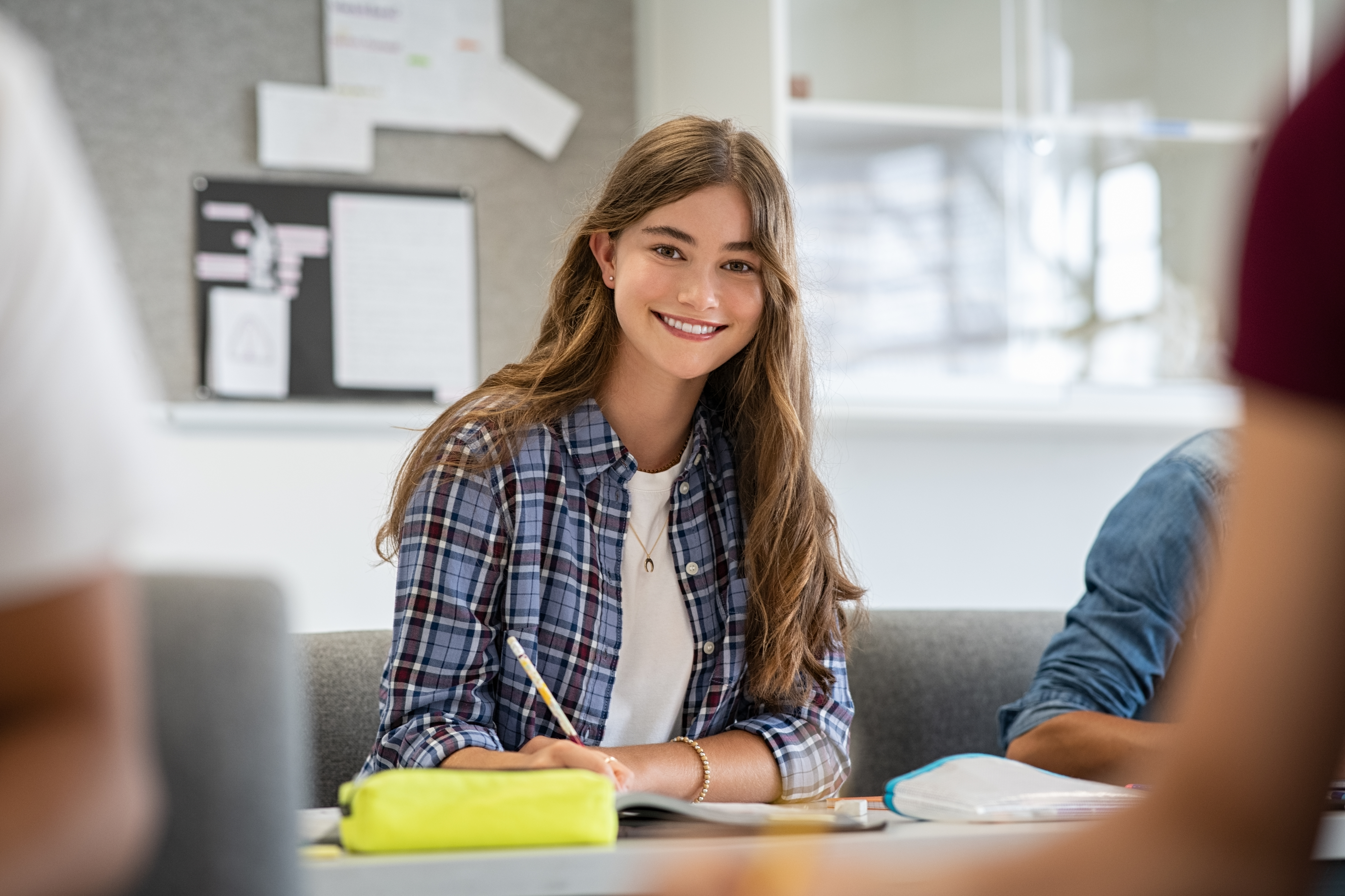 Hermosa estudiante universitaria sonriendo mientras estudiaba para los exámenes en el aula. Linda mujer sentada en un aula llena de estudiantes durante la clase. Retrato de una joven feliz escribiendo notas y mirando a la cámara.