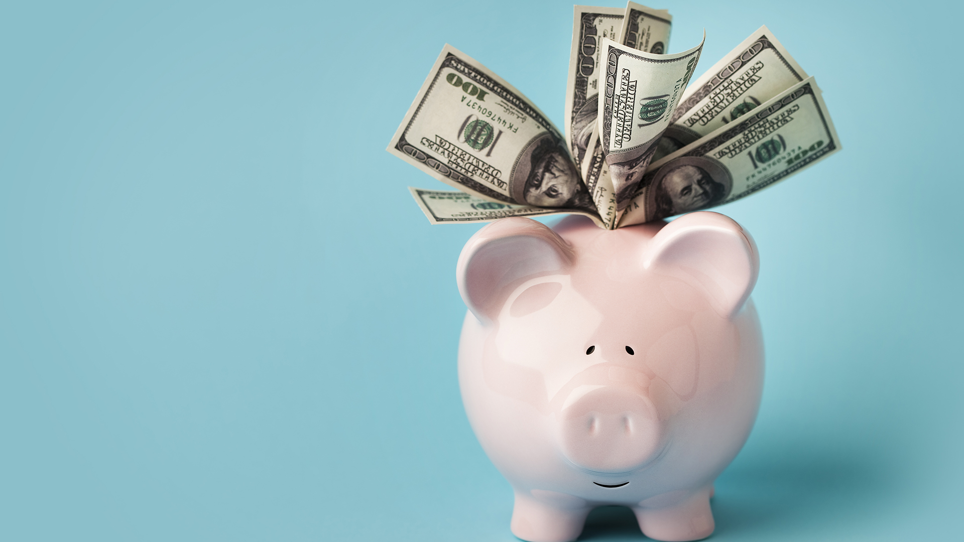 "Una alcancía rosa sonriente llena de billetes de 100 dólares, sobre fondo azul con espacio para copiar. También te puede interesar:"