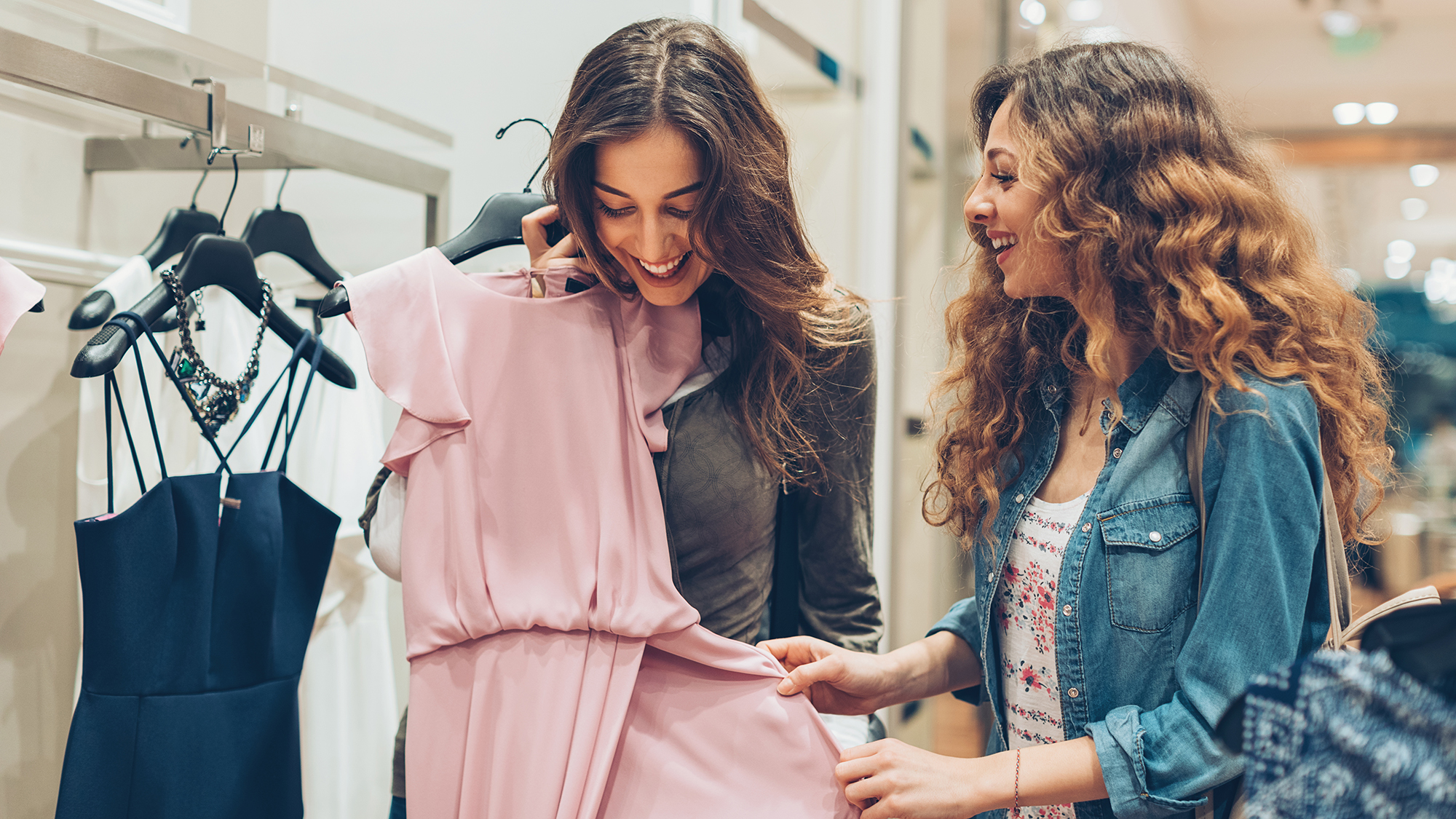 Dos mujeres jóvenes eligiendo vestidos en una tienda de moda de lujo