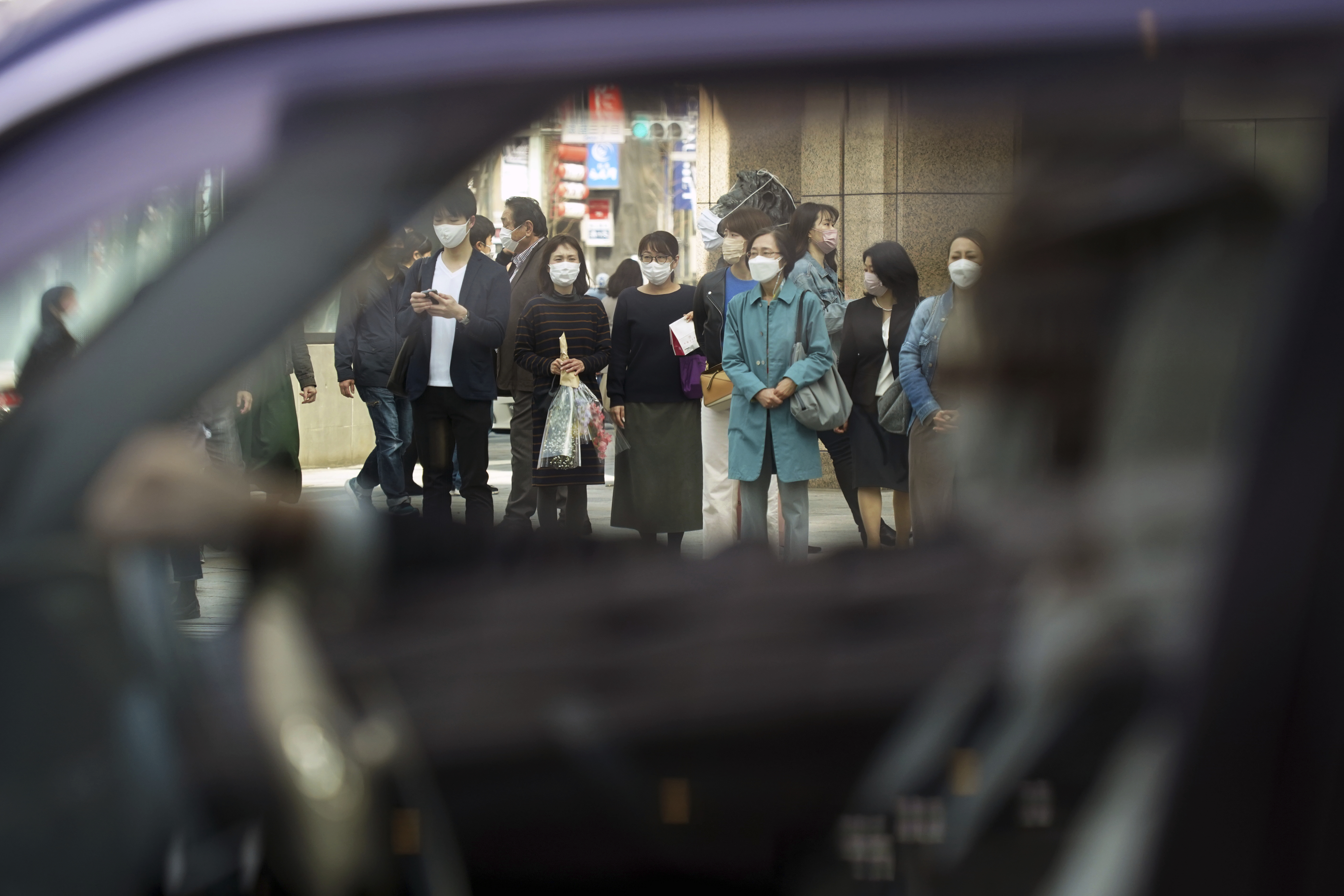 Las personas que usan máscaras protectoras para ayudar a frenar la propagación del coronavirus esperan caminar en un paso de peatones en el distrito comercial de Ginza el miércoles 16 de marzo de 2022 en Tokio. (AP Photo/Eugene Hoshiko)